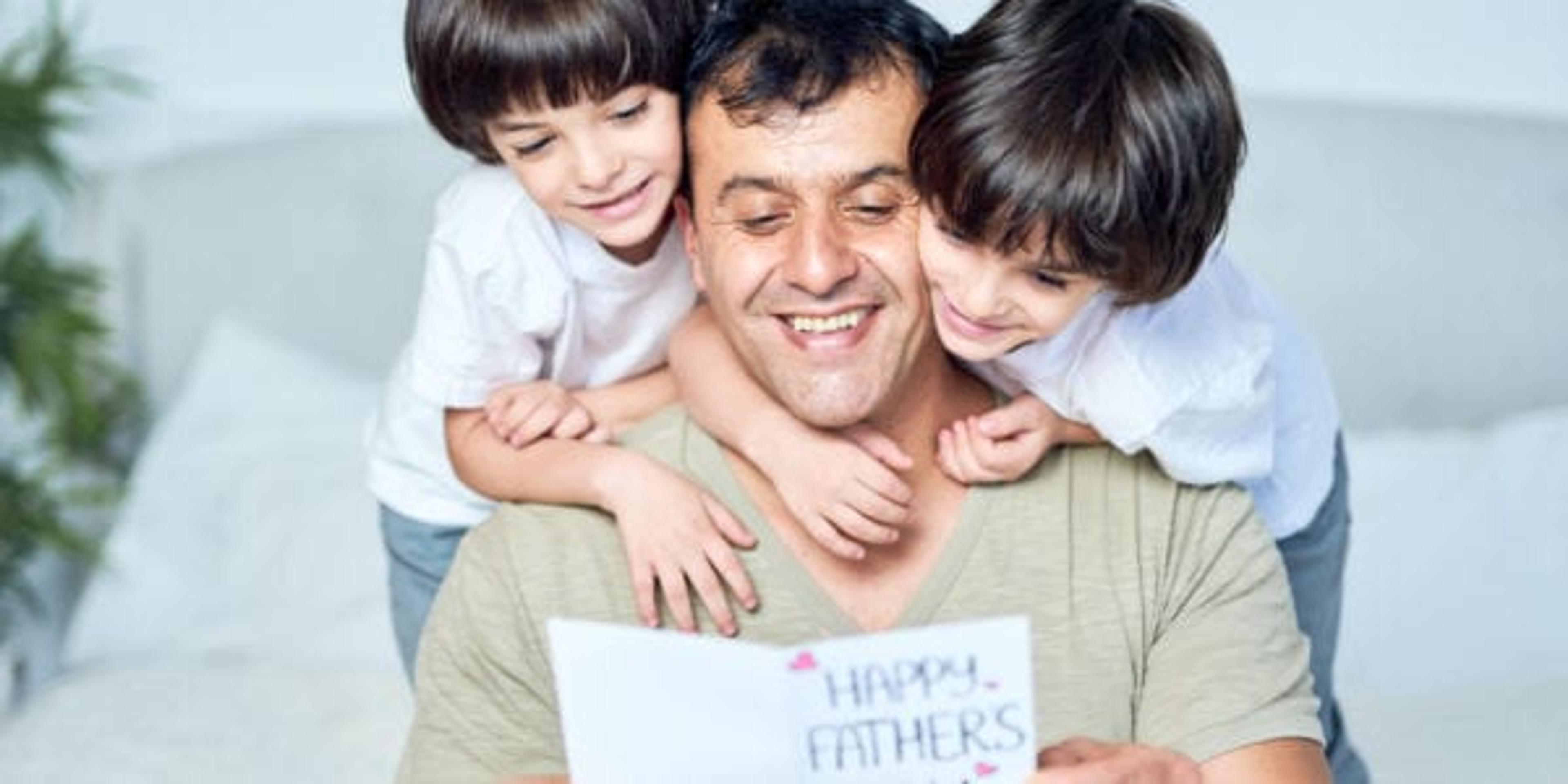 Portrait of latin father looking happy while his two little boys embracing their dad, giving him handmade postcard, greeting with Father's day, spending time together at home. Fatherhood, children