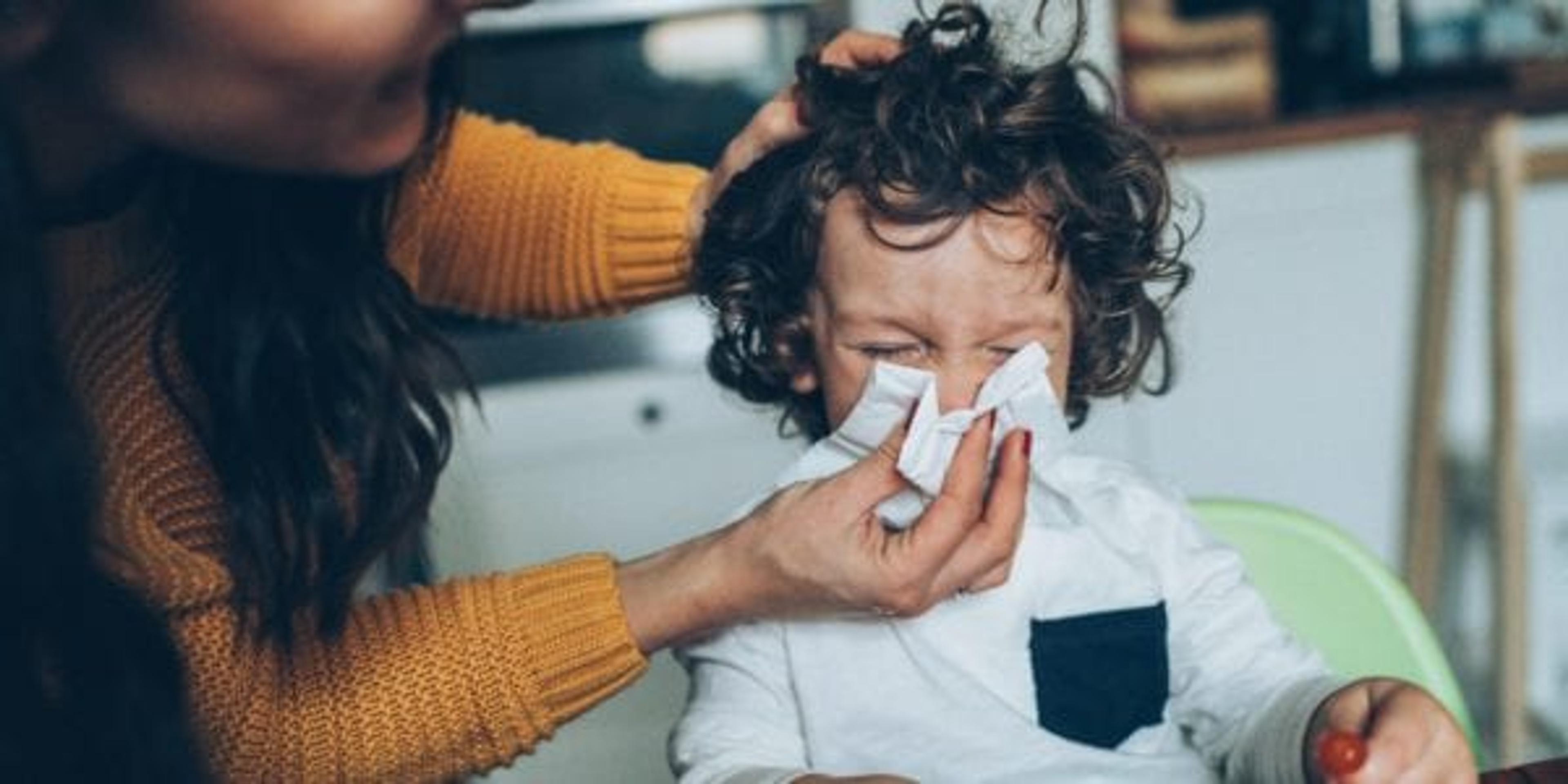 Mom helping a little boy blow his nose.