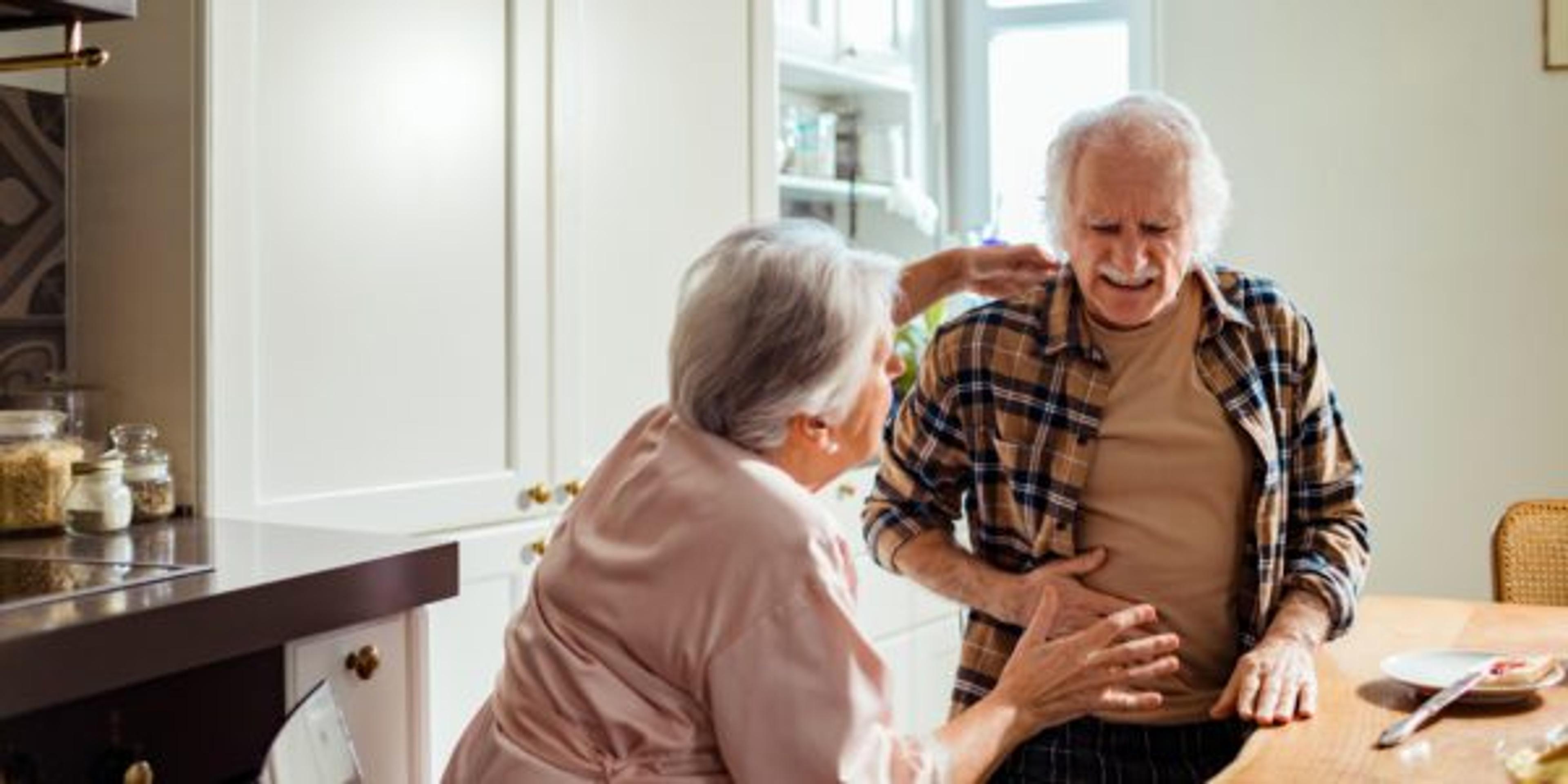 Senior man experiencing stomach pain while having breakfast with his wife