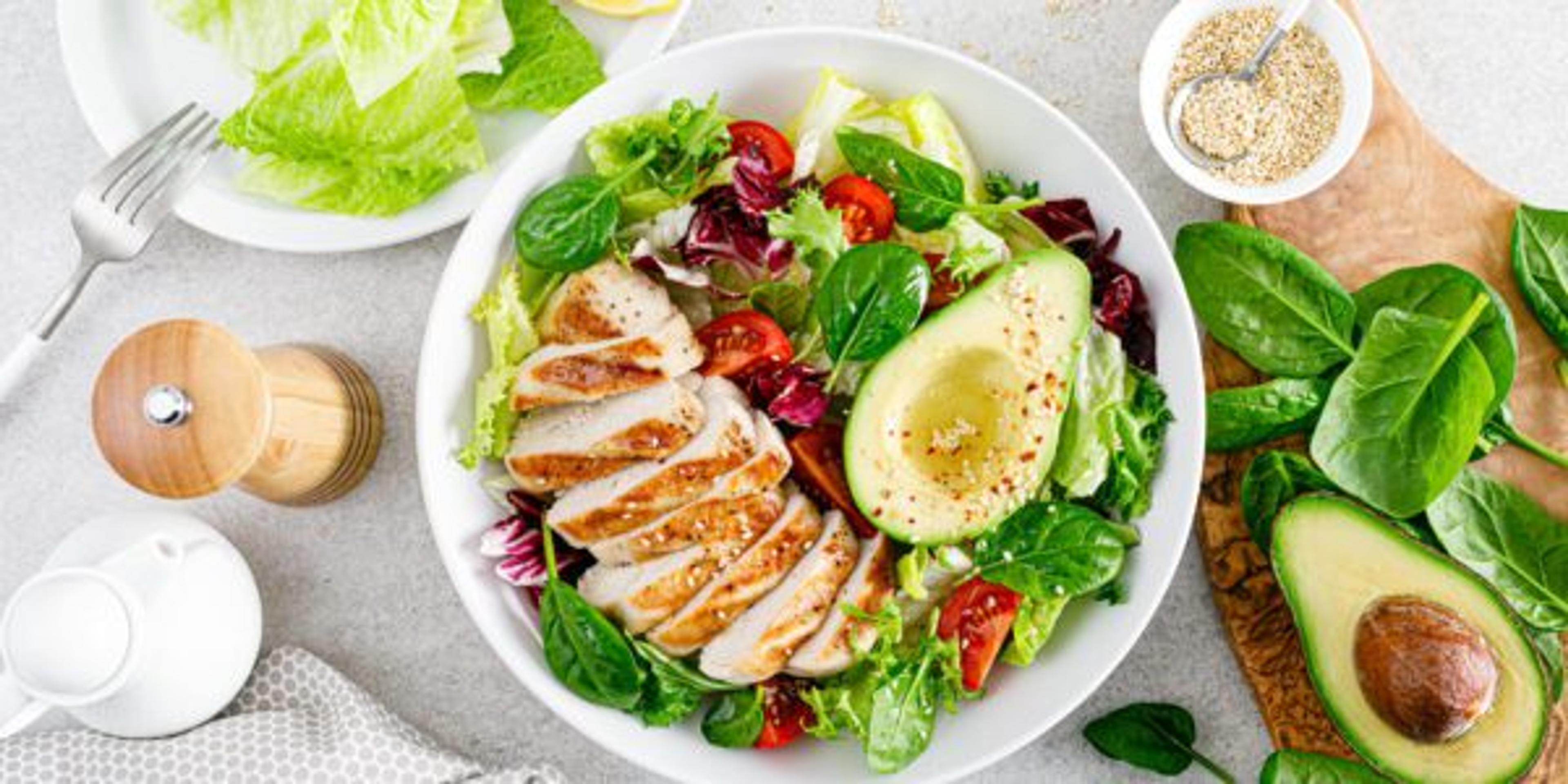 Grilled chicken meat and fresh vegetable salad of tomato, avocado, lettuce and spinach. Healthy and detox food concept. Ketogenic diet. Buddha bowl dish on white background, top view