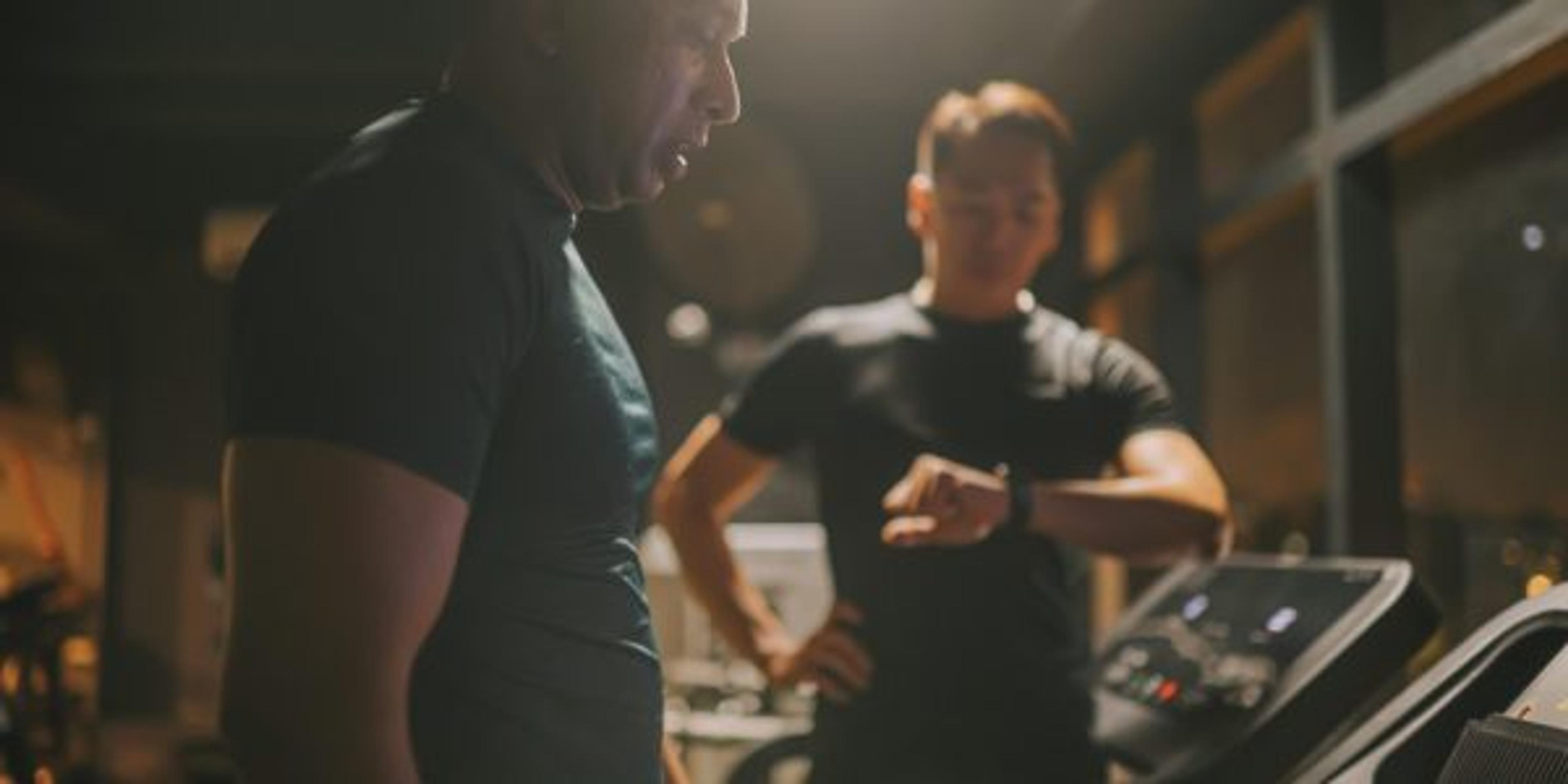 Body Positive Asian Indian man running on treadmill monitored by fitness instructor timing