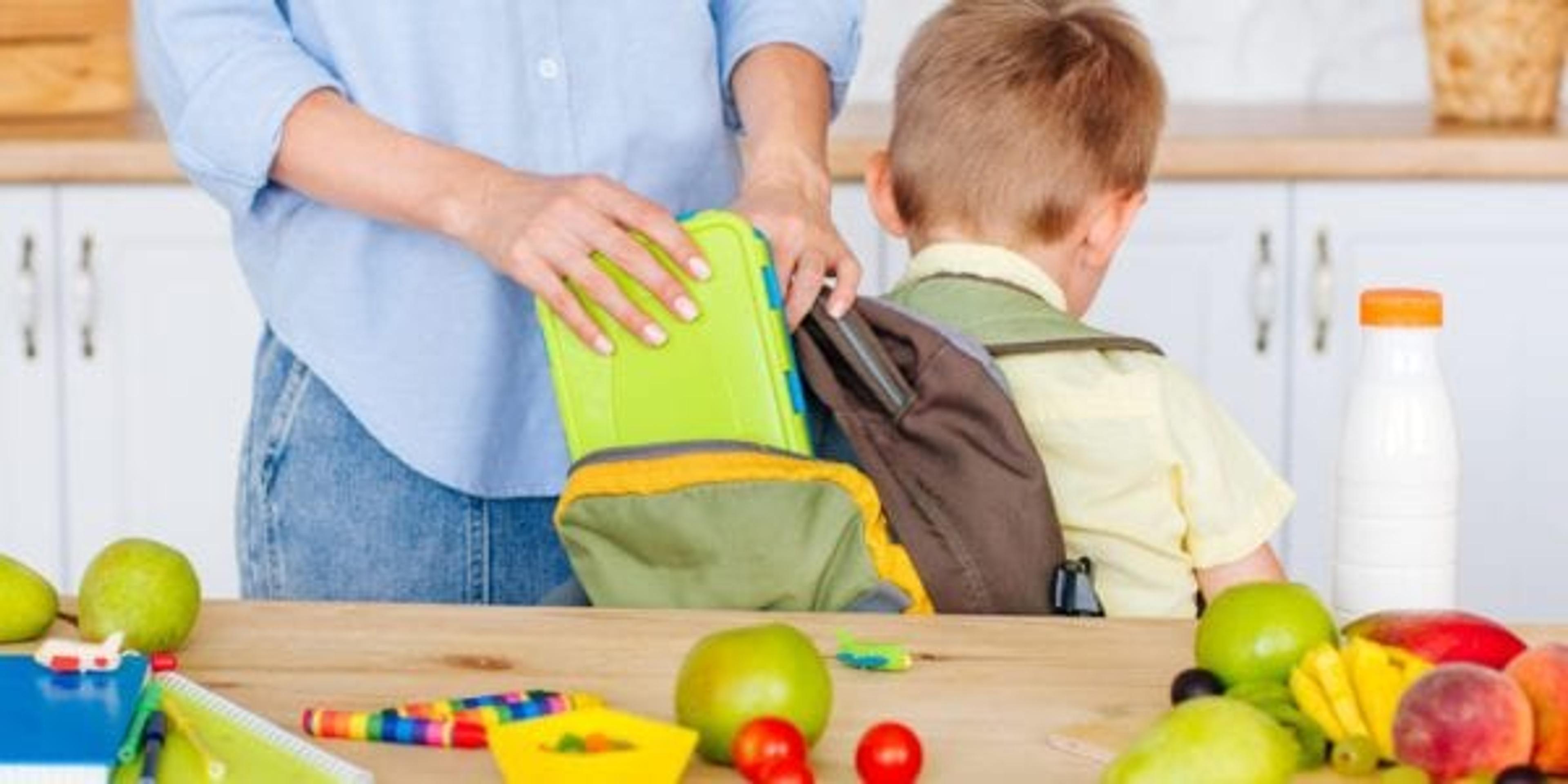 Closeup view of mother putting lunch box into her son's backpack