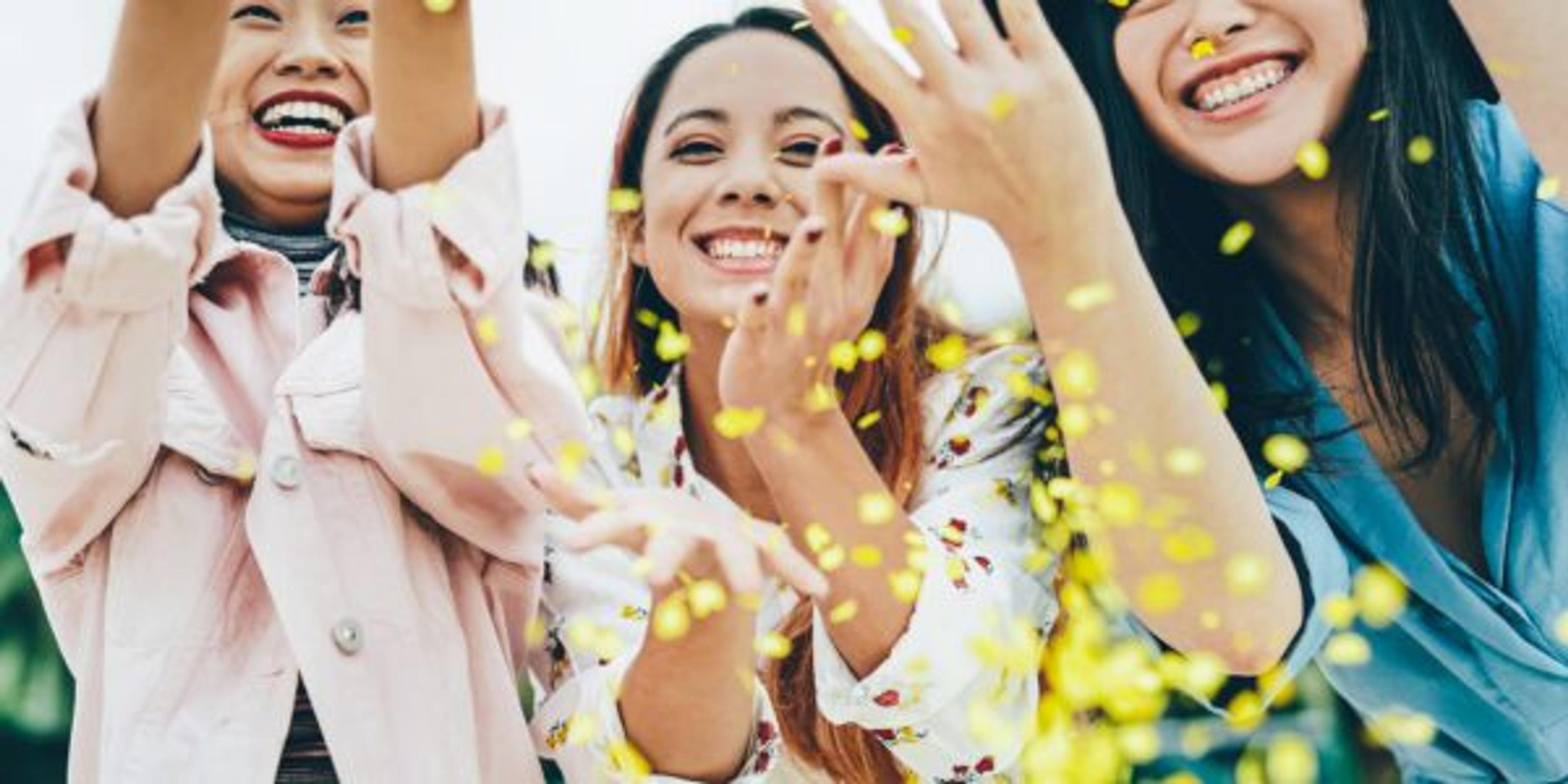 Happy Asian friends having fun throwing confetti outdoor - Young trendy people celebrating at festival event outside - Party, entertainment and youth holidays lifestyle concept