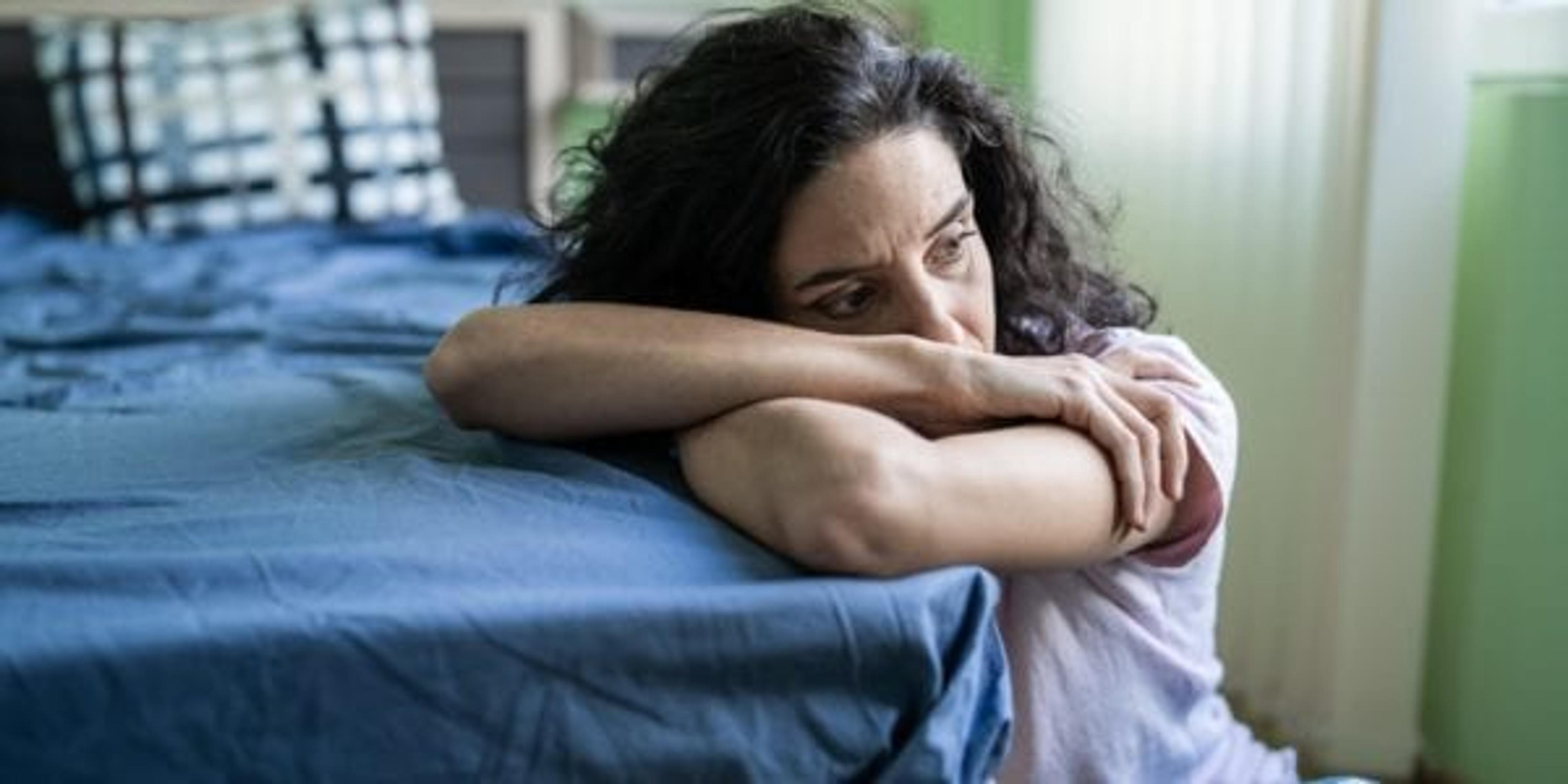 Woman with head on arms sitting by bed