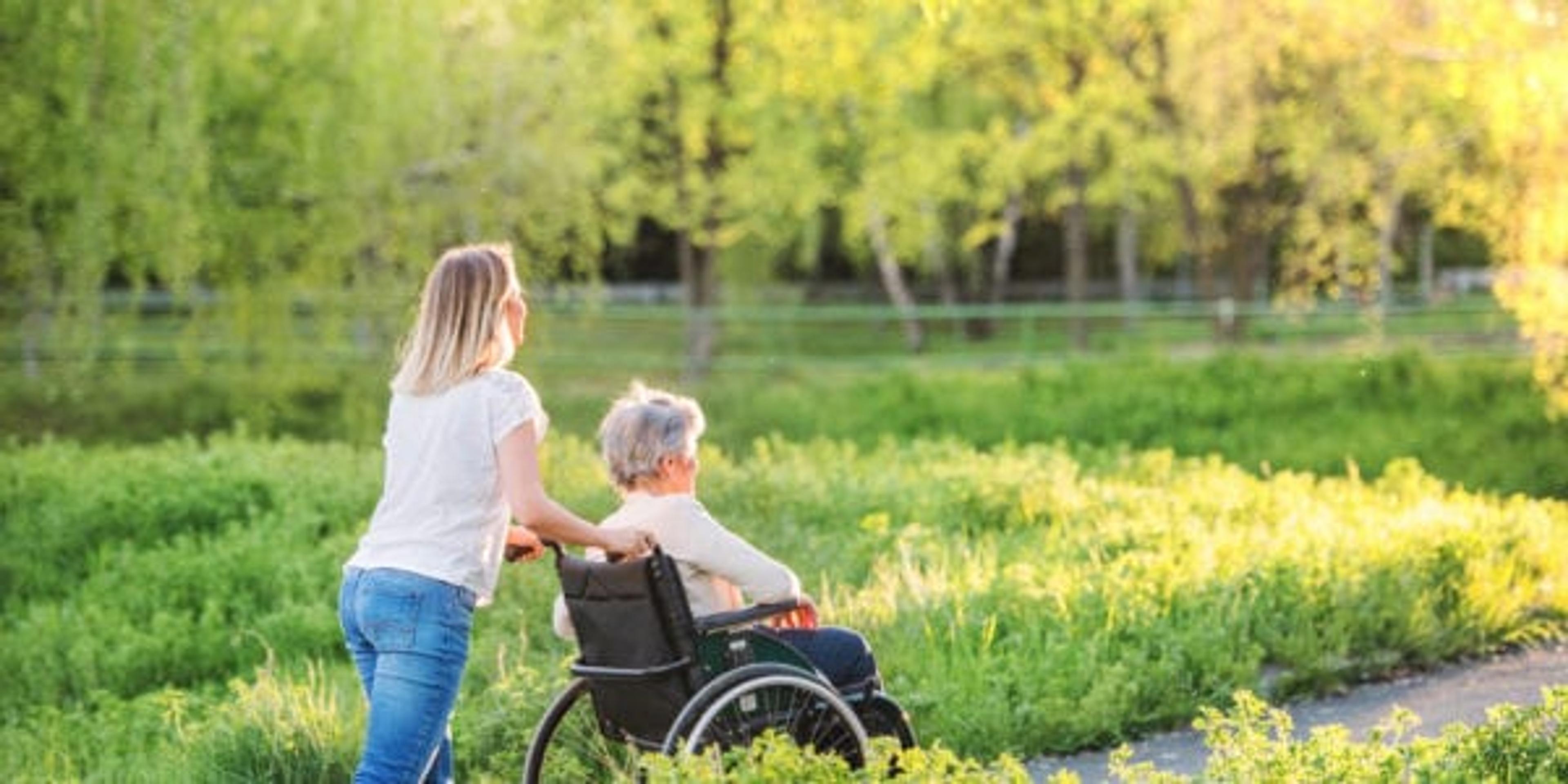 Elderly grandmother in wheelchair with an adult granddaughter outside in spring nature.