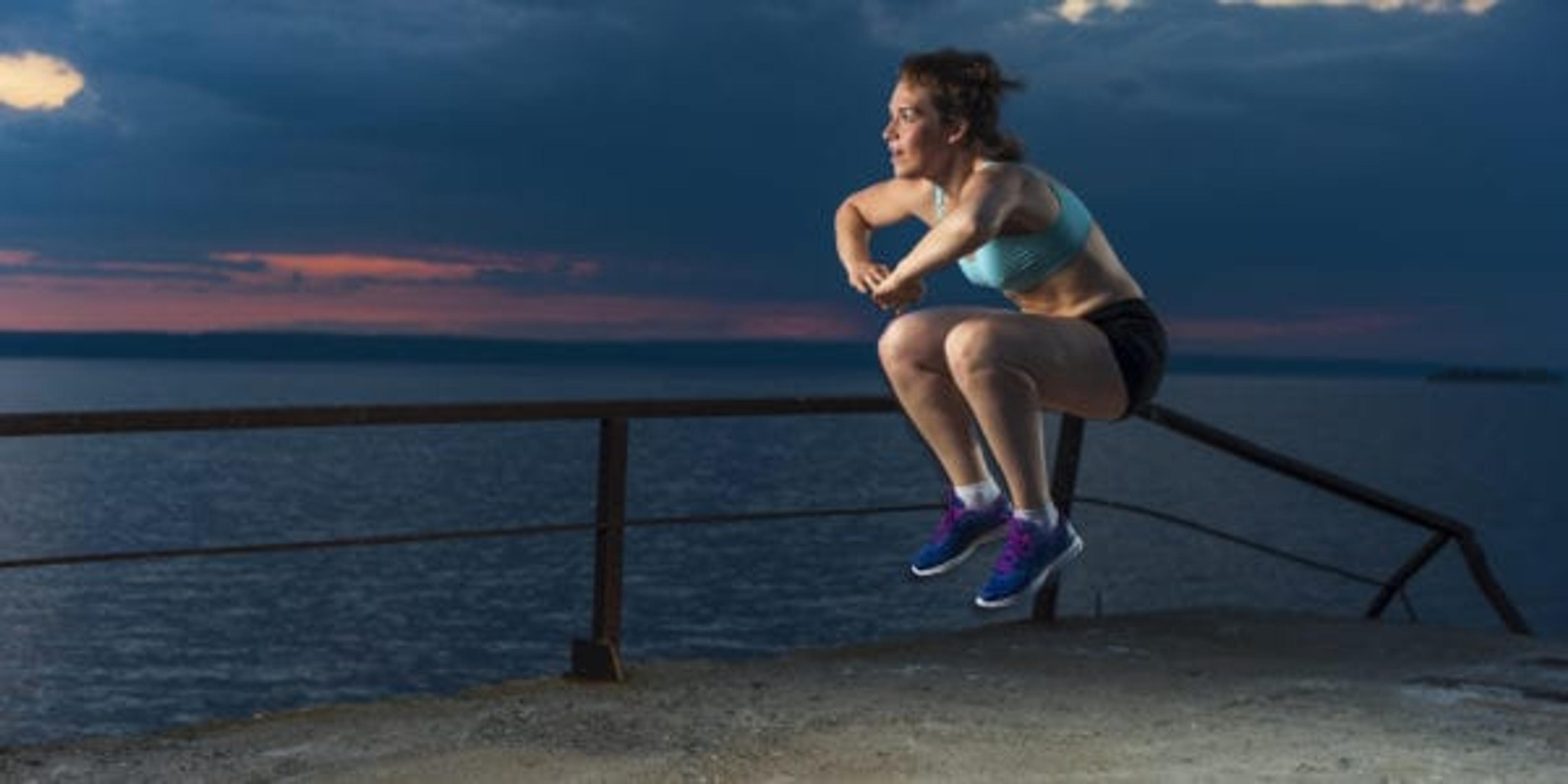 Young caucasian woman in sportswear doing plyometric exercises on pier. Fitness workout outdoors