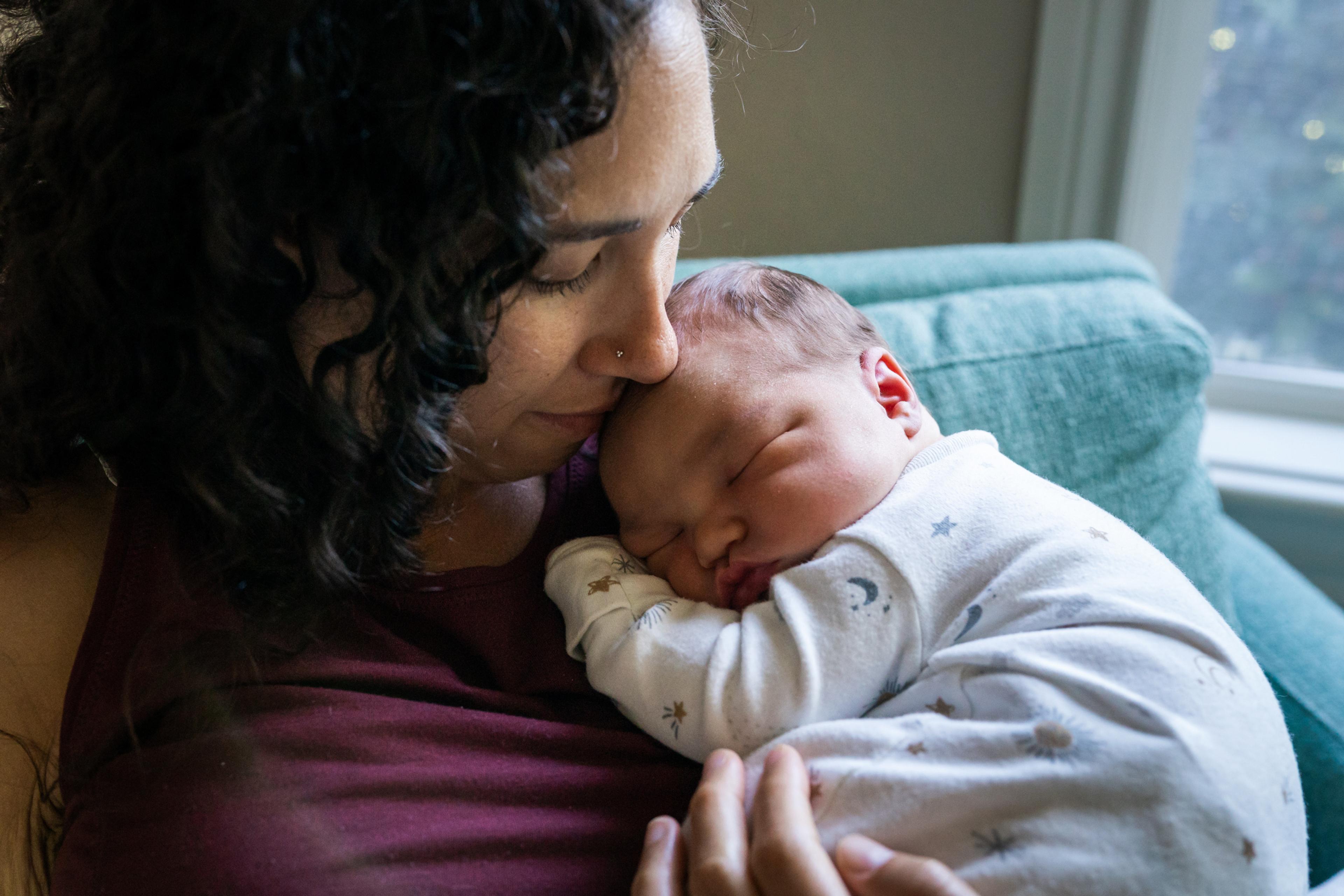 A new mother is comforting her sleeping newborn on her shoulder.