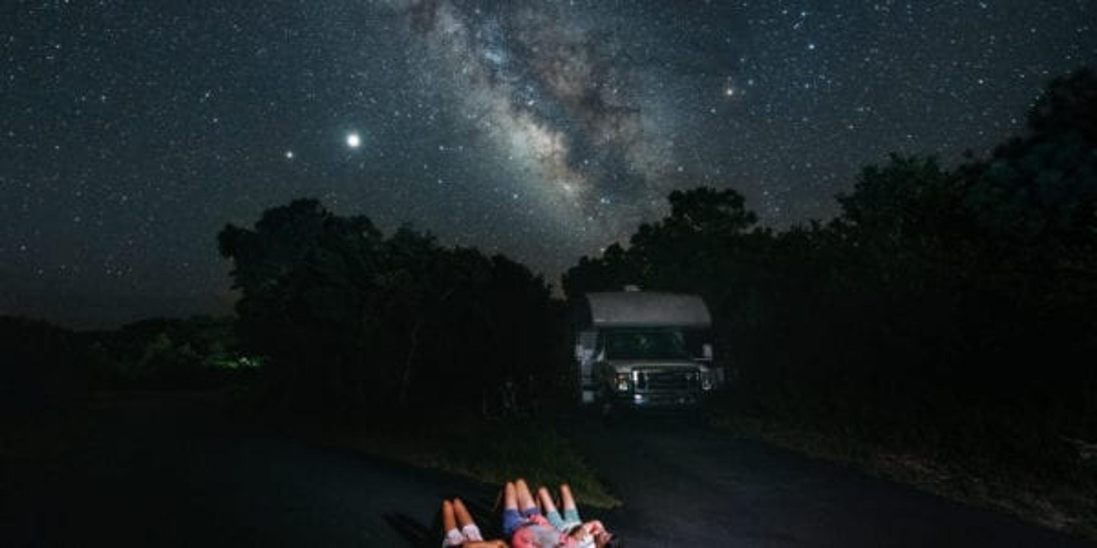 Family lies on the ground by RV looking at the stars