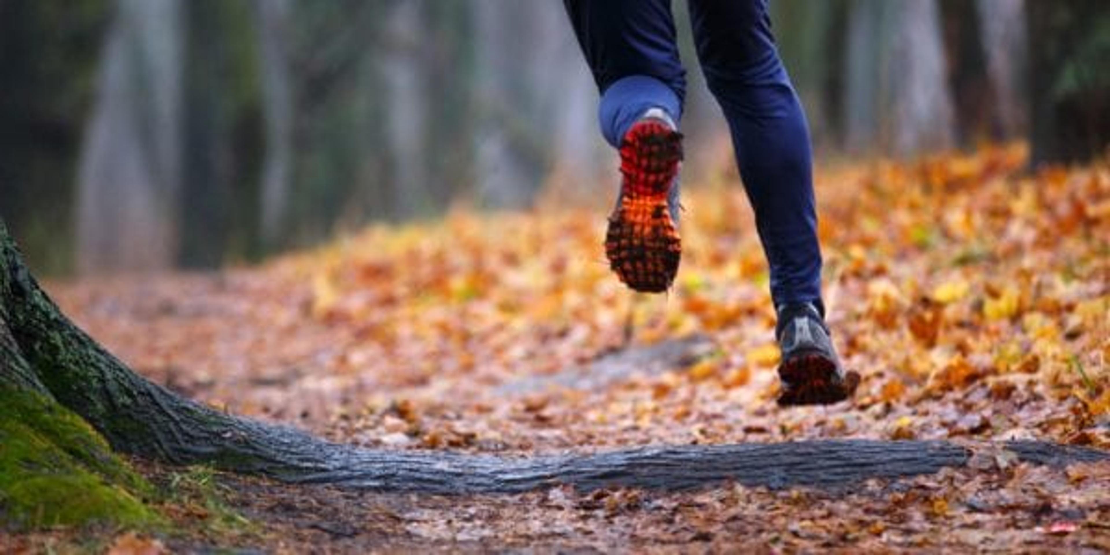 Runner on trail filled with autumn leaves