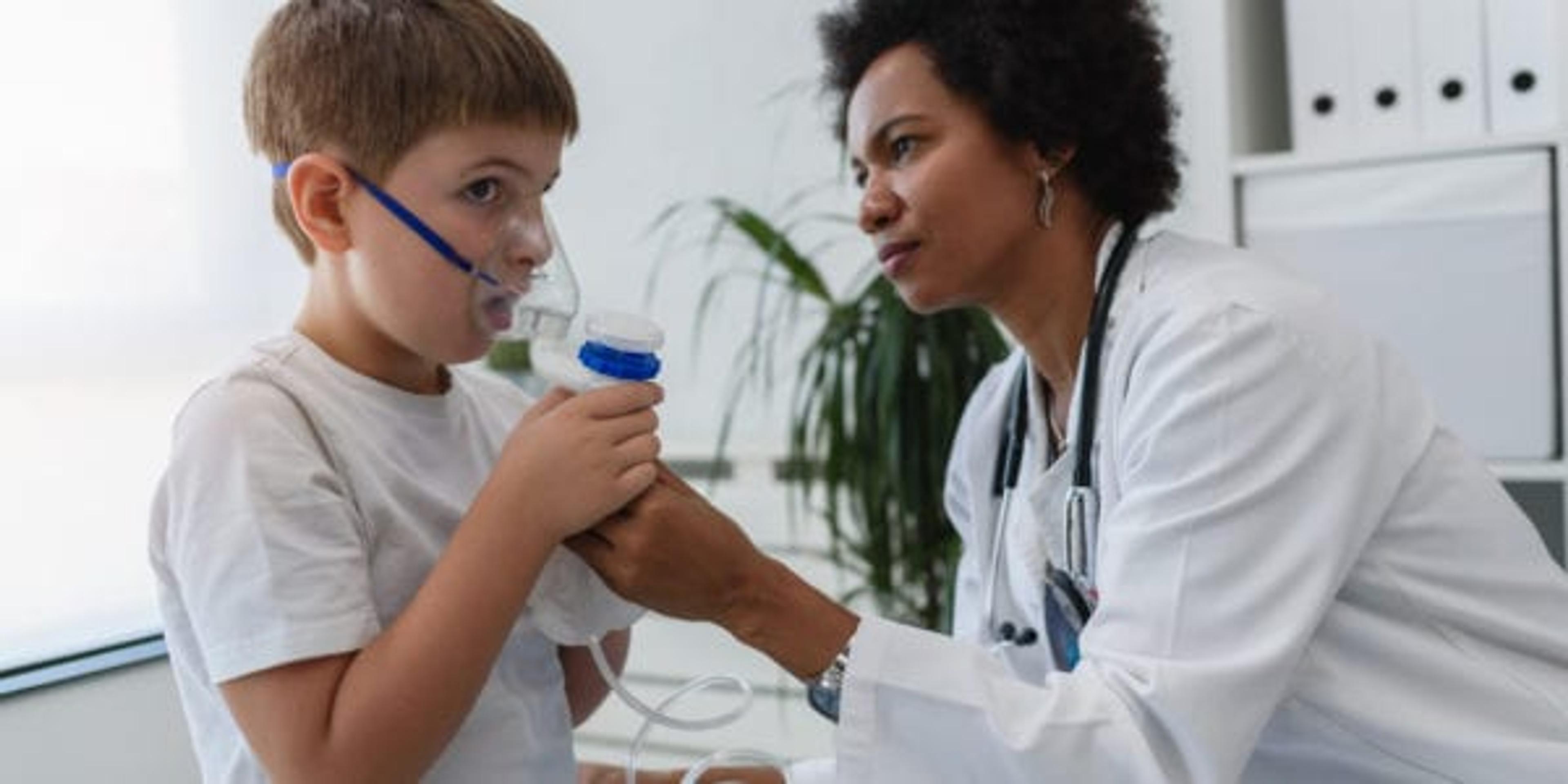 Woman African American doctor general practitioner helping child to put nebulizer inhaler face mask. Asthma treatment for children.