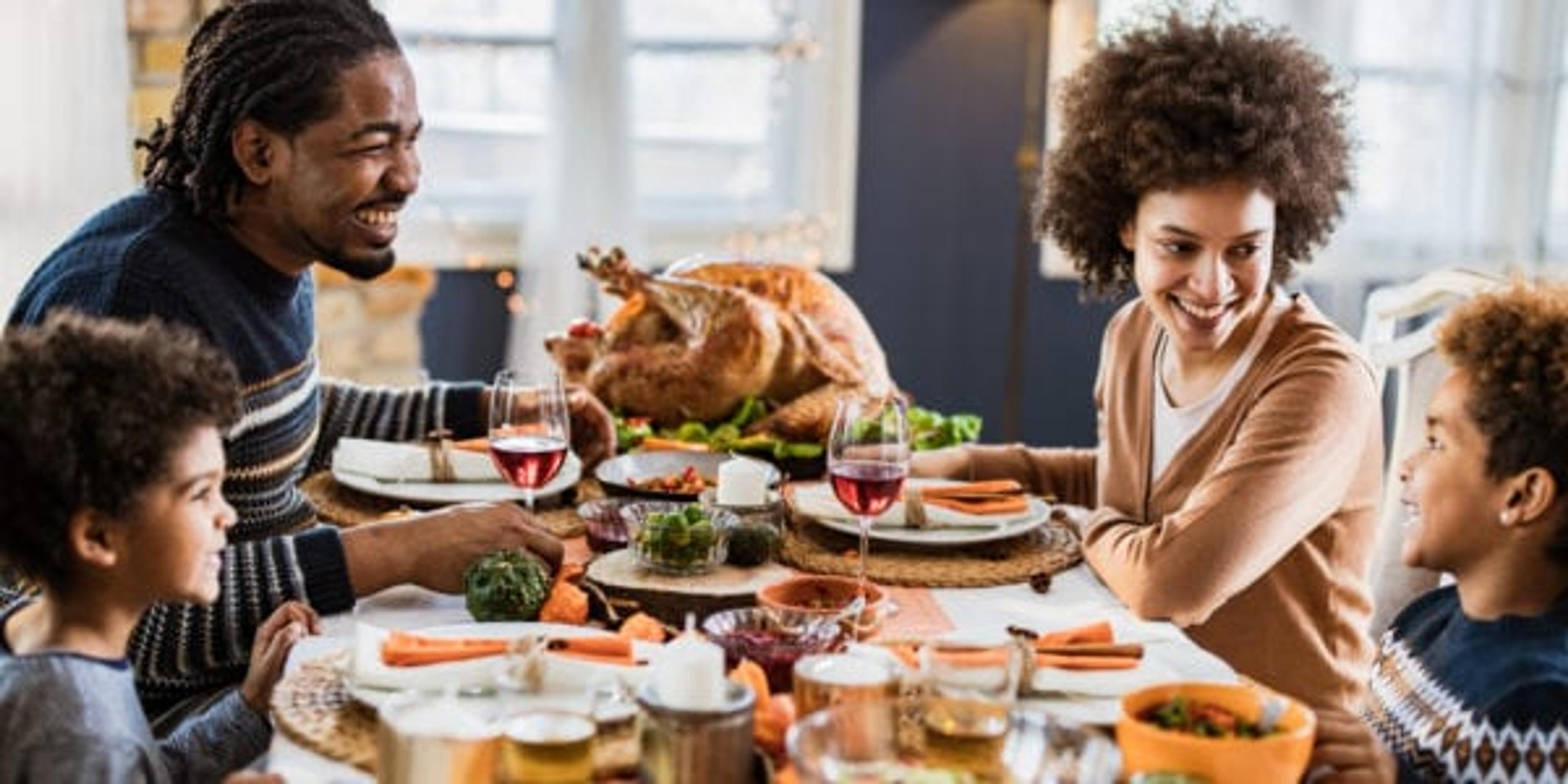 Happy black family talking during Thanksgiving meal at dining table.