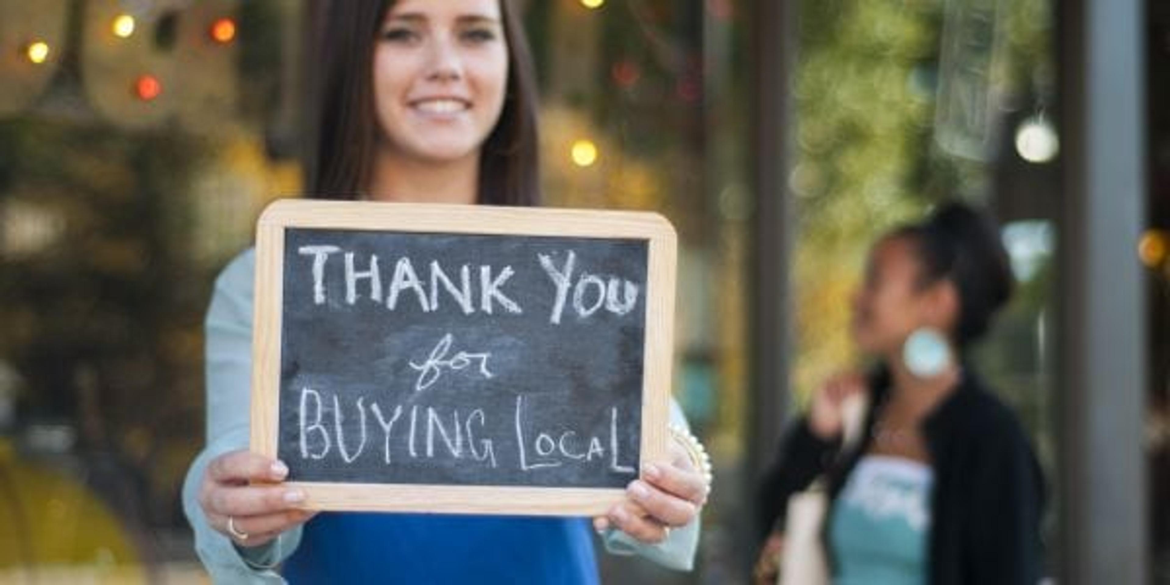 Woman holding "thank you for buyng local" sign