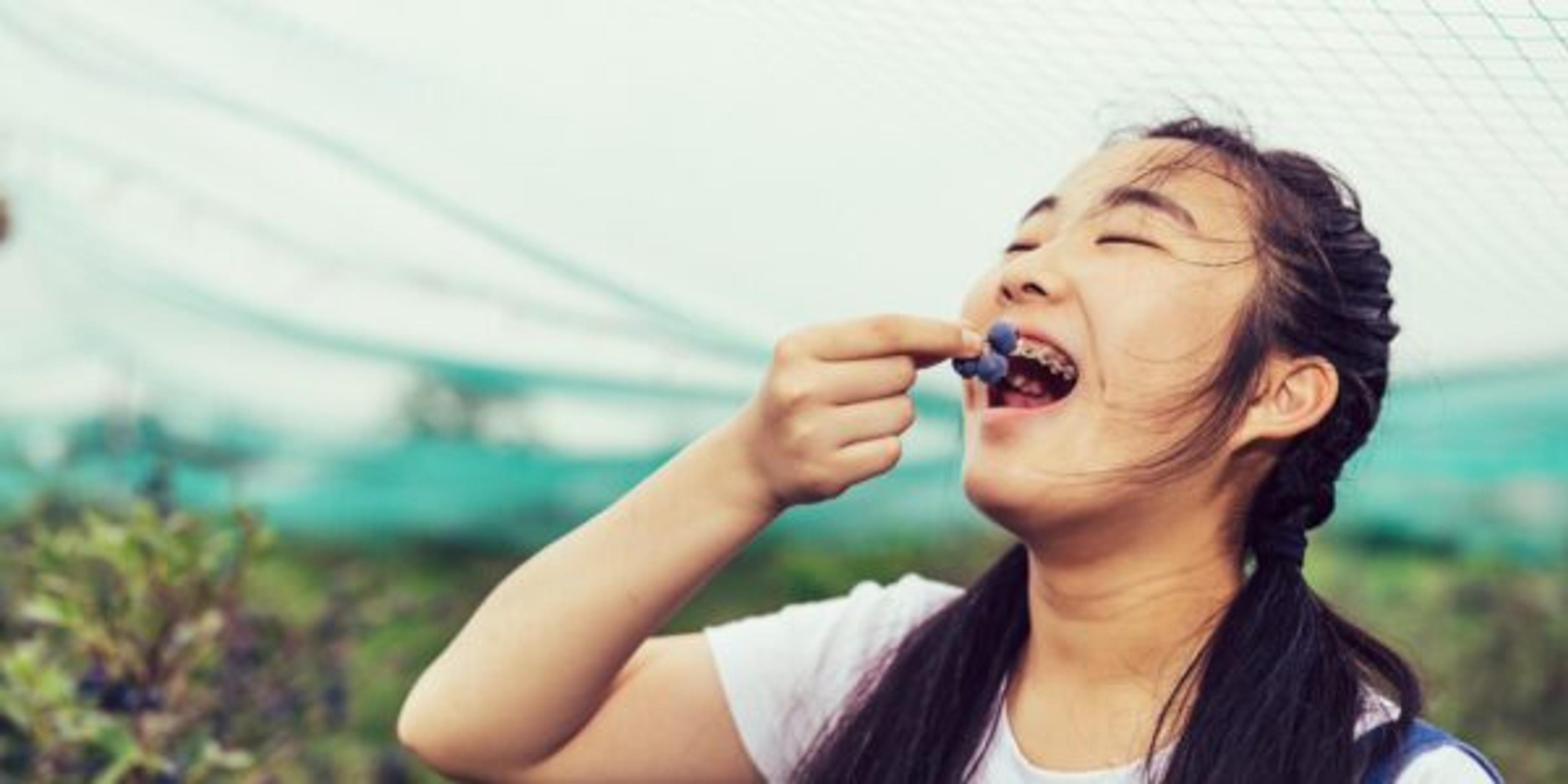 Asian Teenager girl eating fresh blueberry and looking at the camera happily from farm