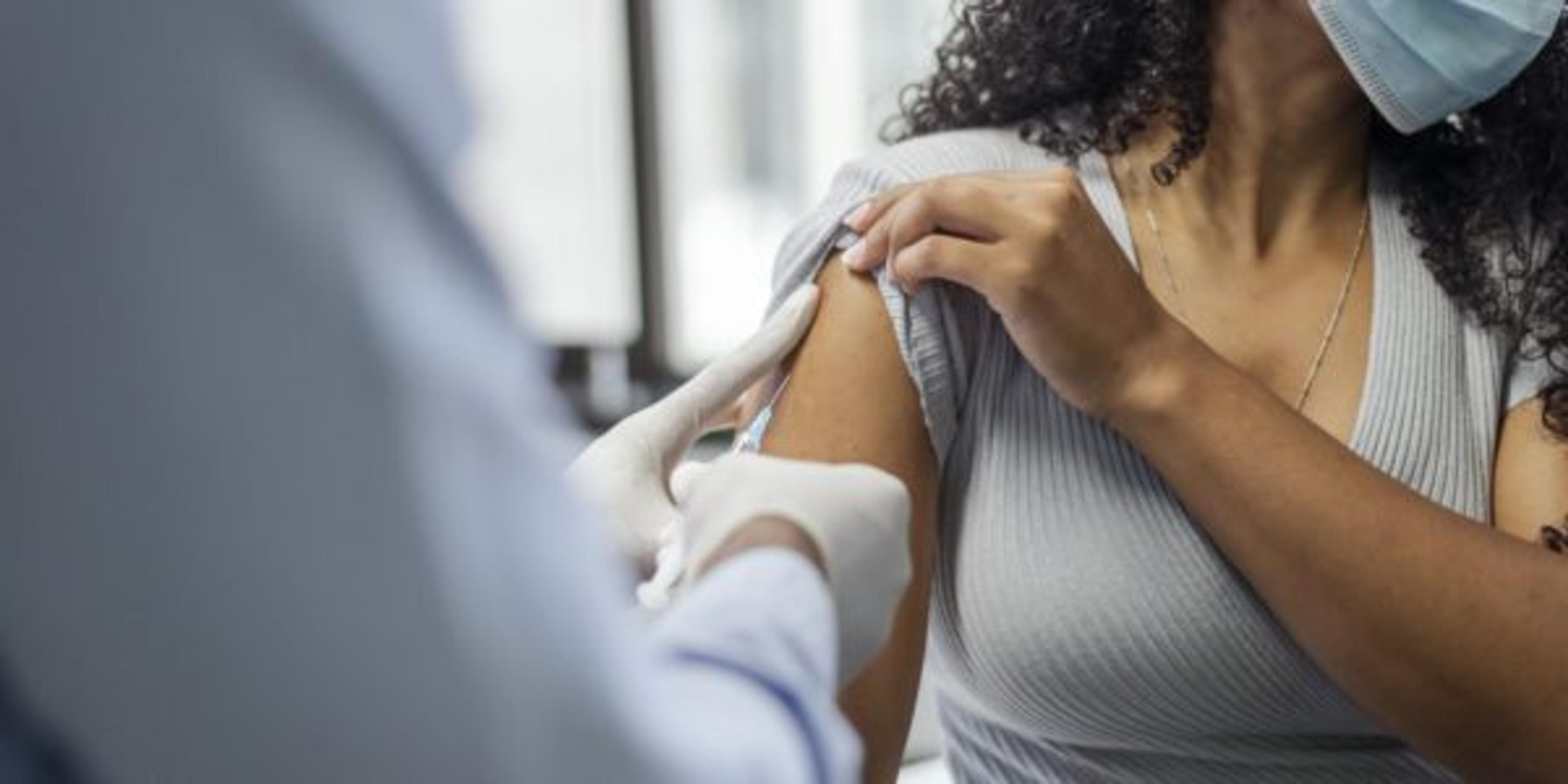 Close up shot of healthcare worker injecting black female patient with COVID-19 vaccine. The woman is wearing a face mask and looking in the opposite direction of the needle.