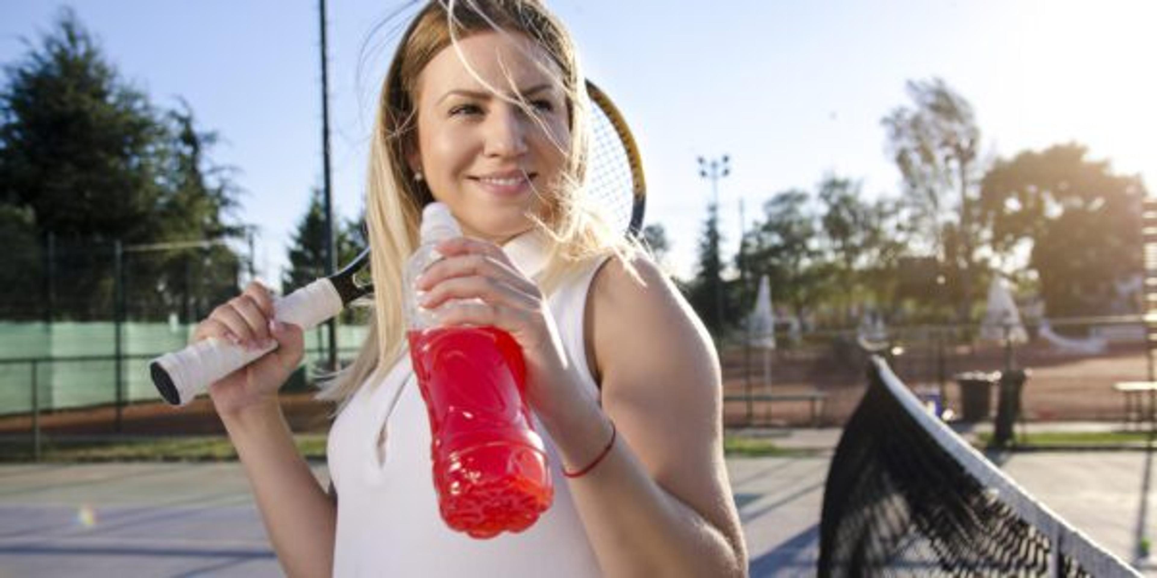 Gorgeous young female tennis player drinking energy drink