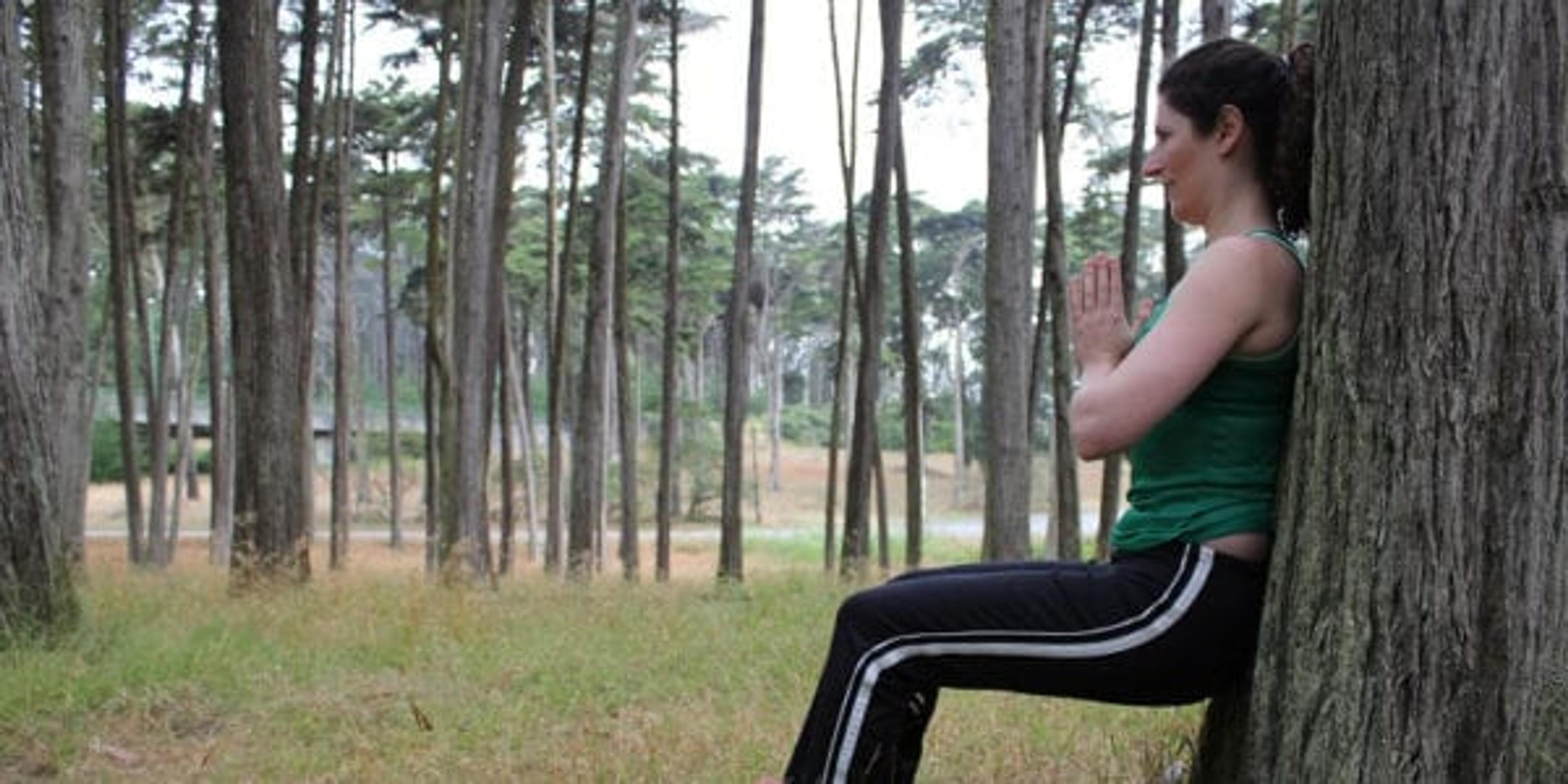 Woman doing a wall sit on a tree.