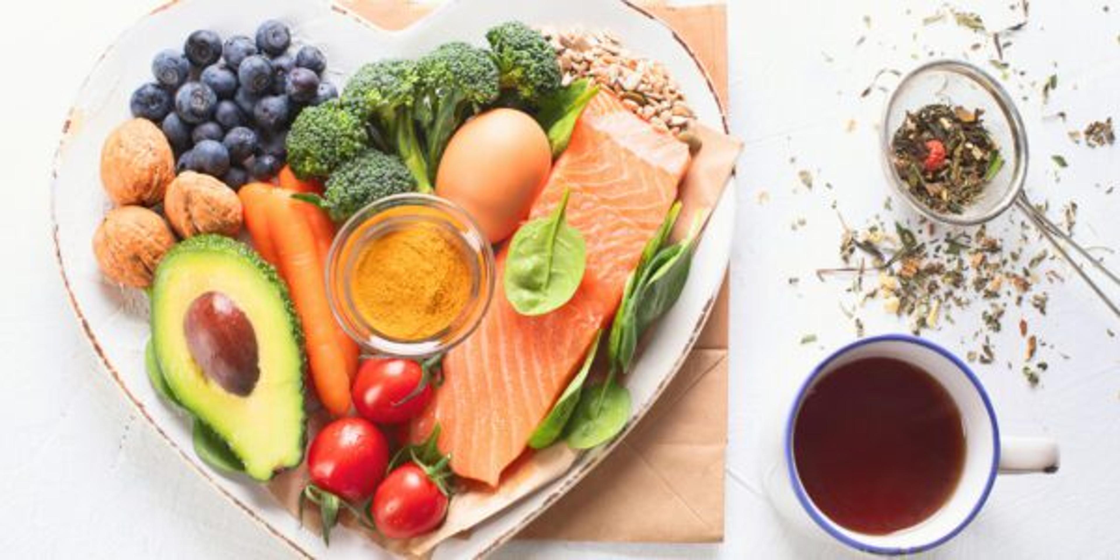 A heart-shaped bowl full of healthy foods like avocado, berries, fish and more.