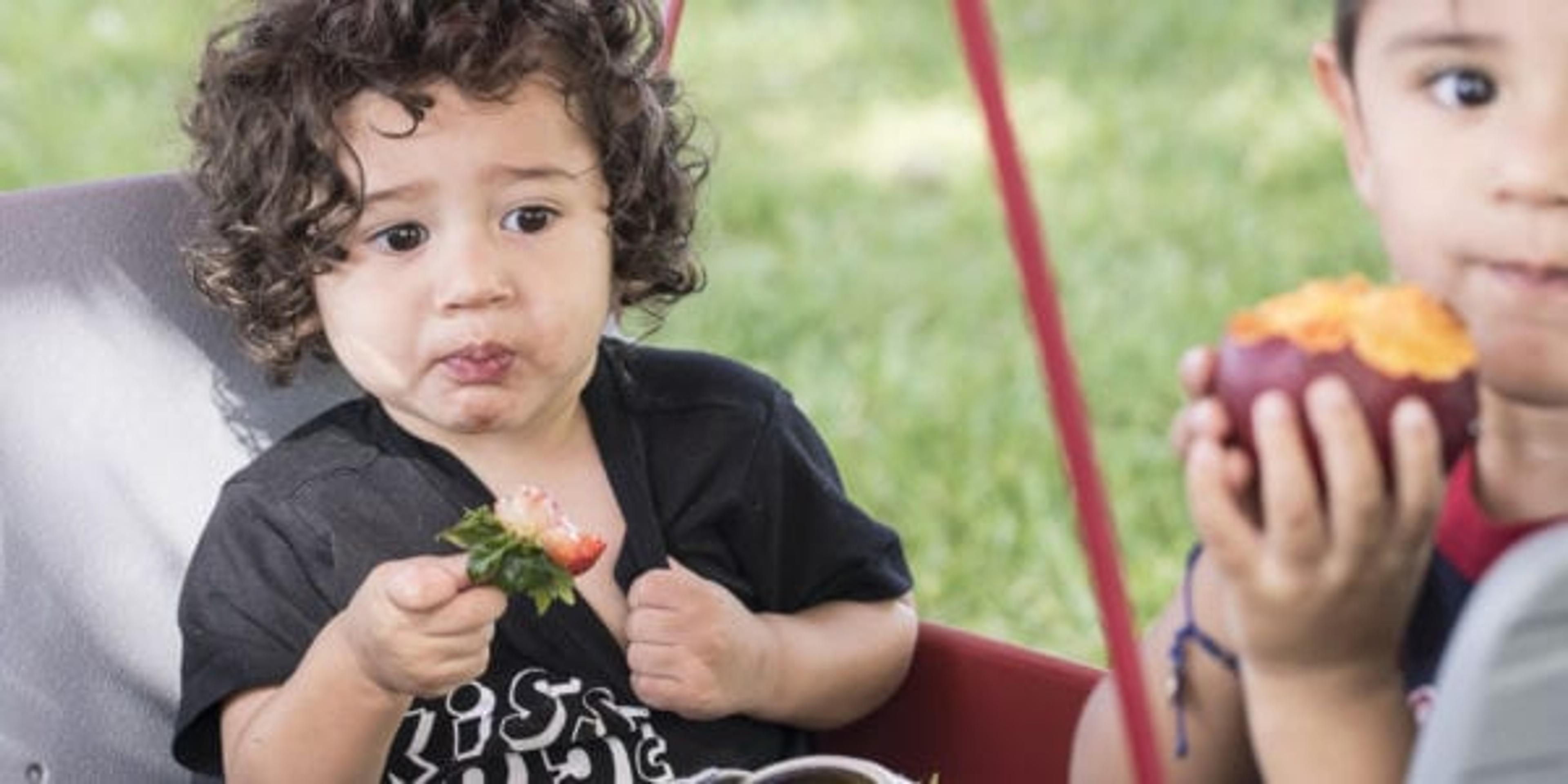 Image of two boys in a wagon, eating a strawberry and peach.