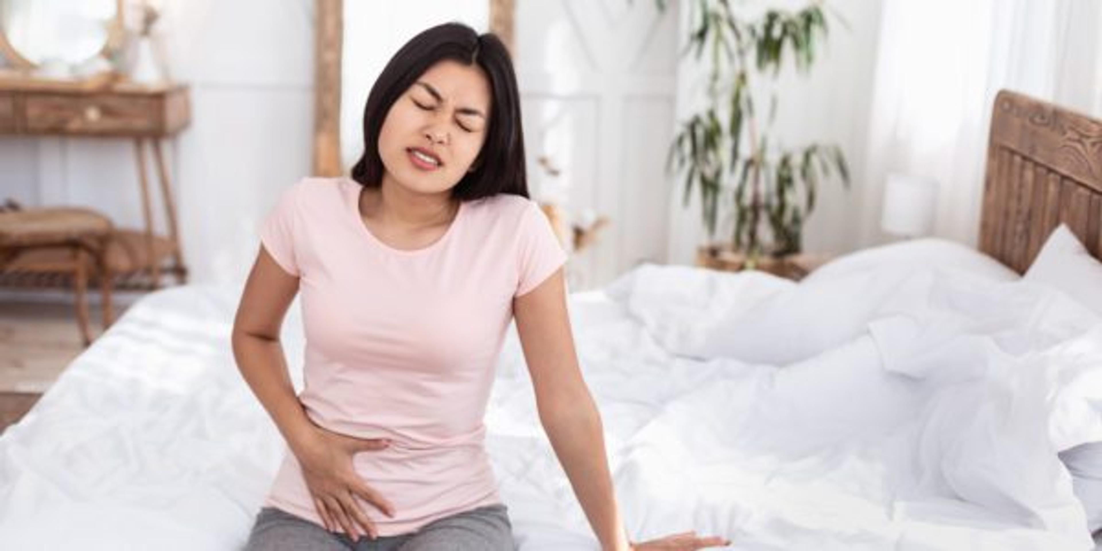 Chinese Girl Having Lower Abdominal Pain Sitting In Bed Indoors