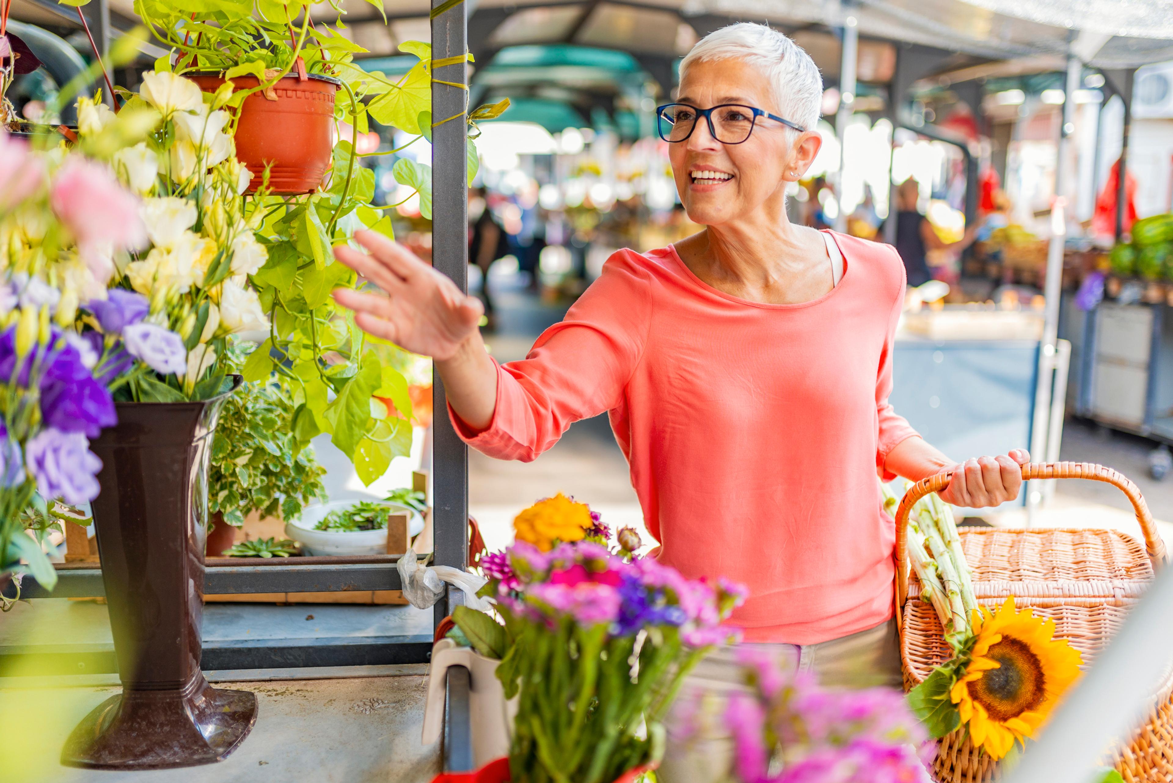 A lady with short white hair is picking out flowers at an outdoor spring market.