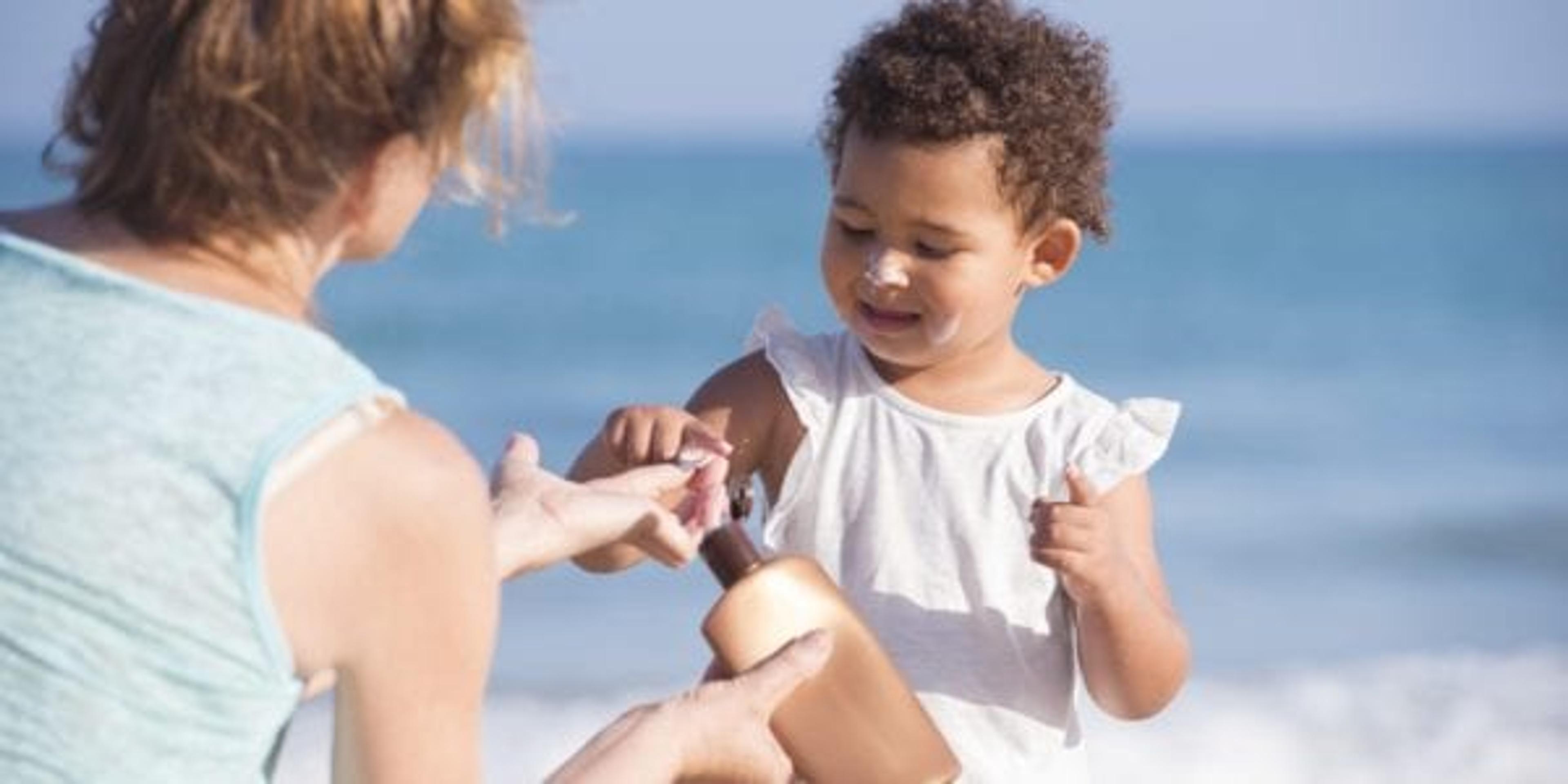 mom putting sunscreen on child at beach