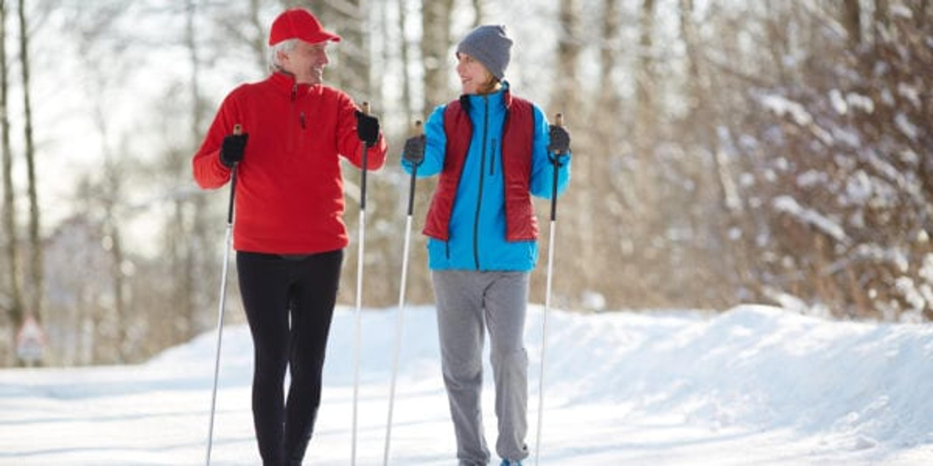 Two active seniors in sportswear trekking down forest road on frosty winter day