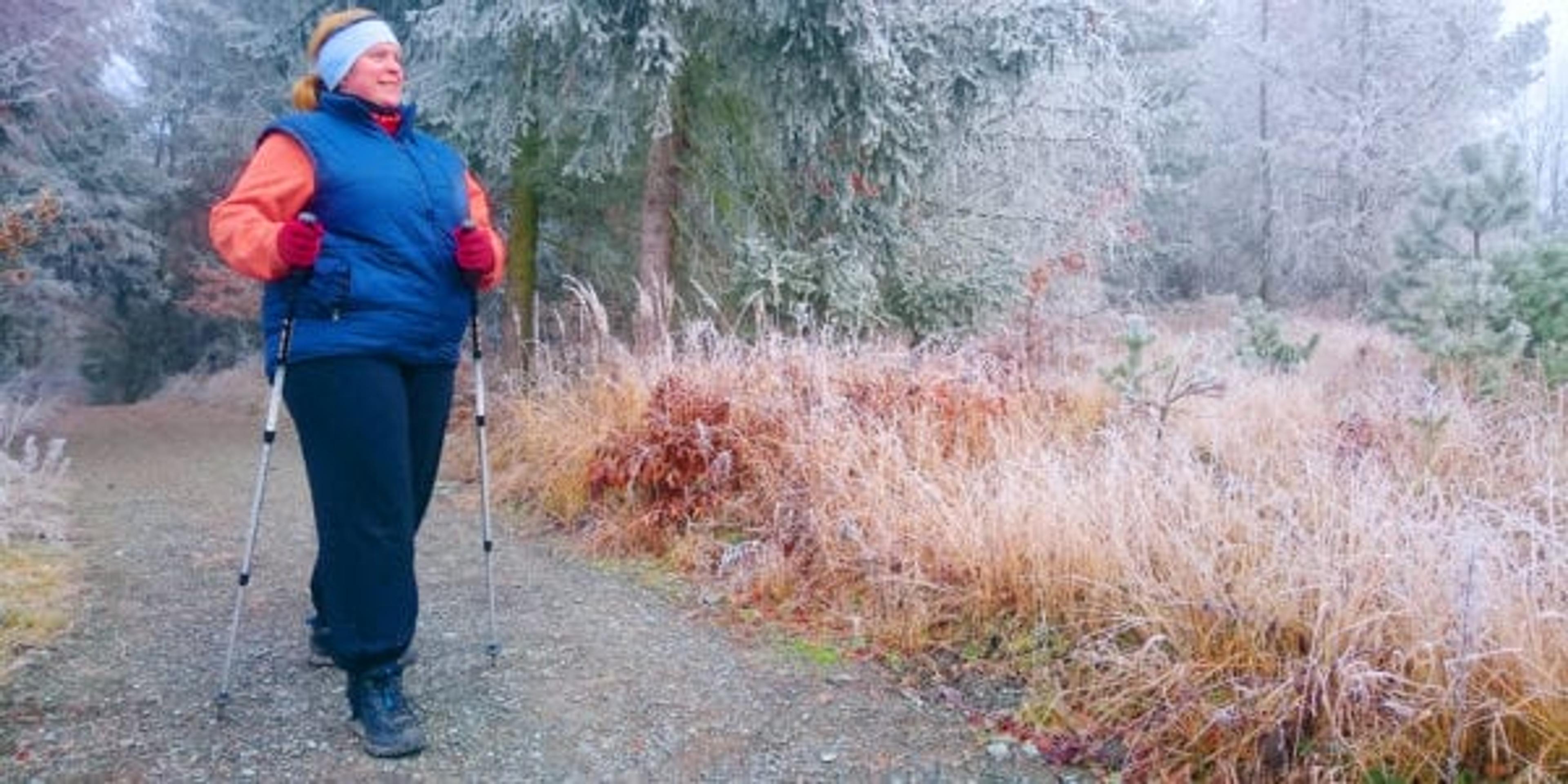 Overweight woman has done New Year resolution for weight loss in new year. Obese hiker walking on forest trail in winter cold weather. Nordic walking in Czech National Park Sumava.