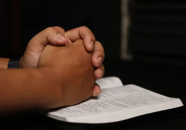 Clasped hands resting on an open Bible