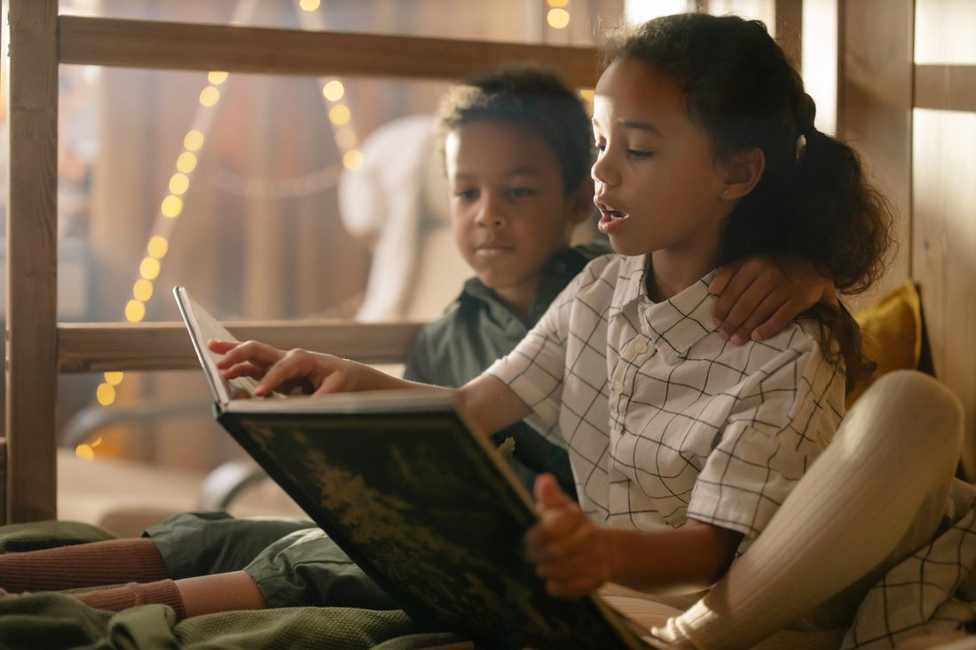 Two children reading a book together by warm lights
