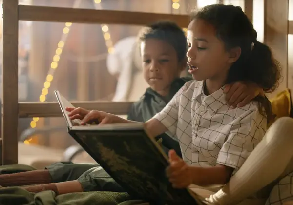 Two children reading a book together by warm lights