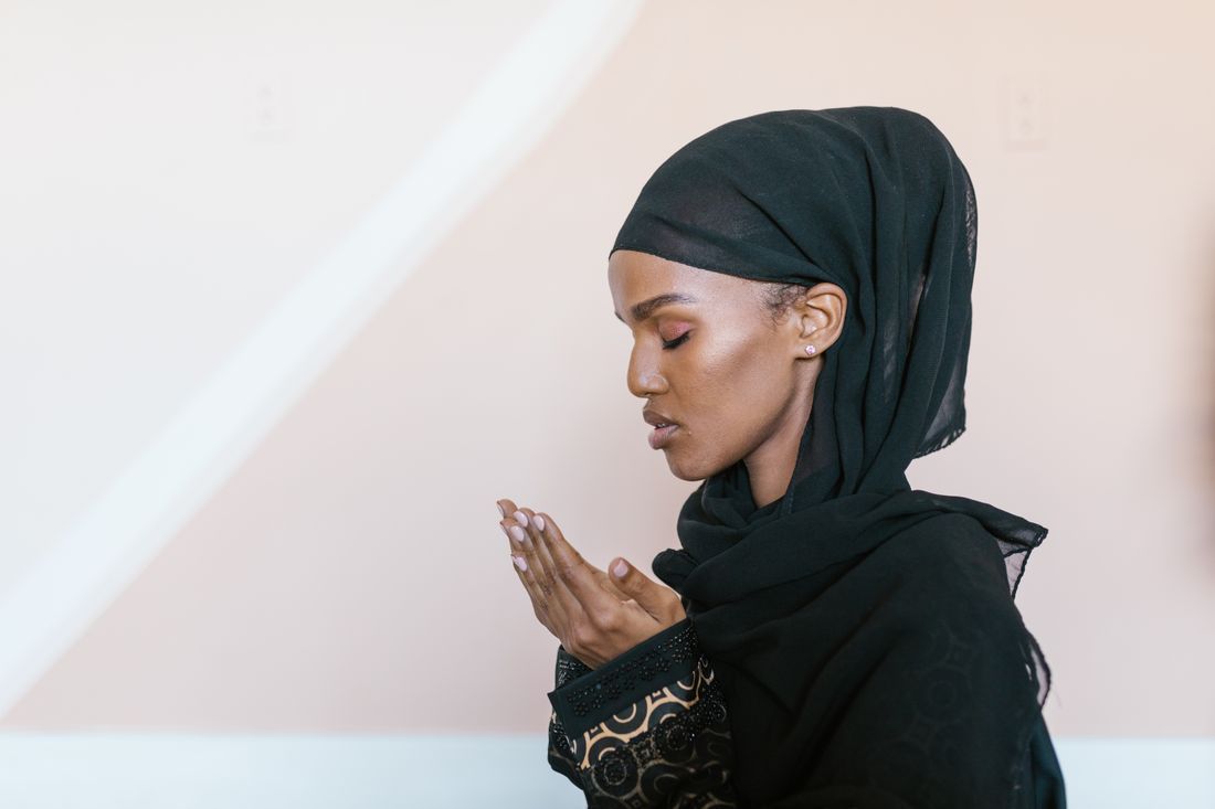 A woman in hijab praying with her hands raised, eyes closed