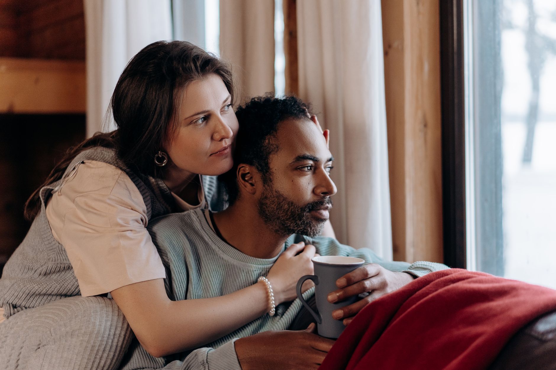 A couple sitting close together by a window with coffee
