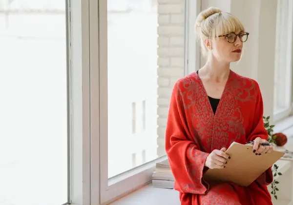 A woman leader with a clipboard pausing by a bright window