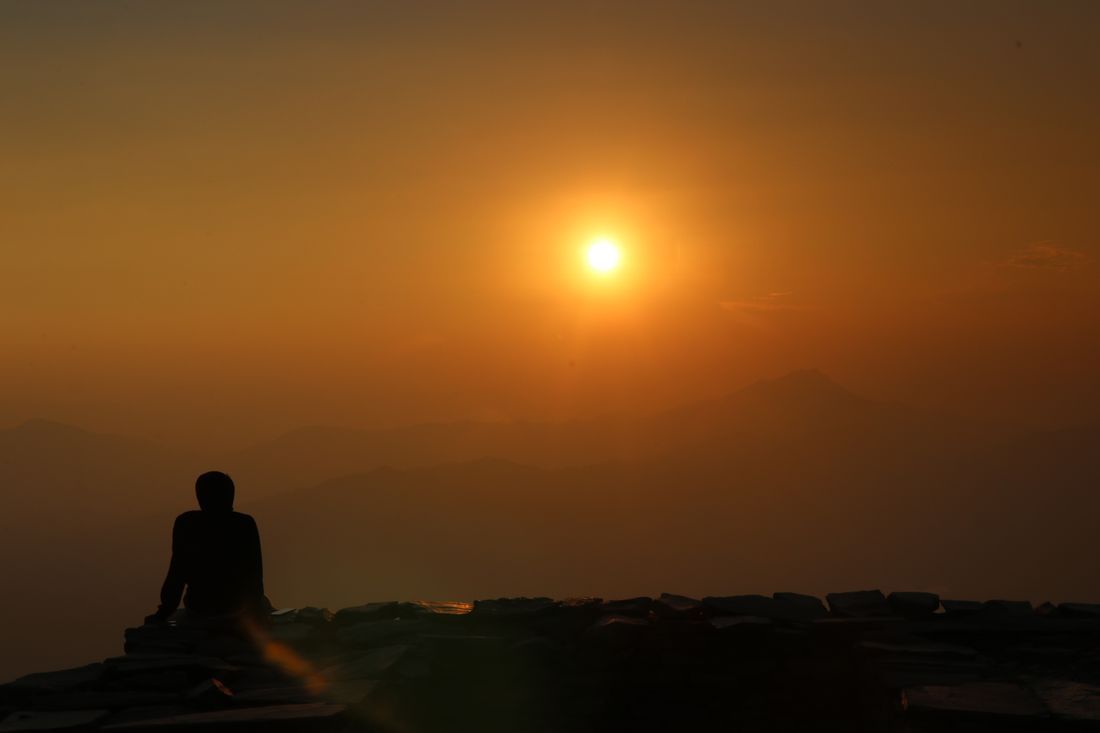 A person watching the sunrise over distant peaks