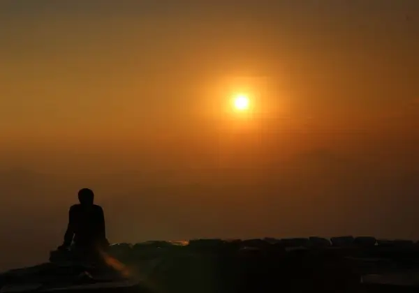 A person watching the sunrise over distant peaks