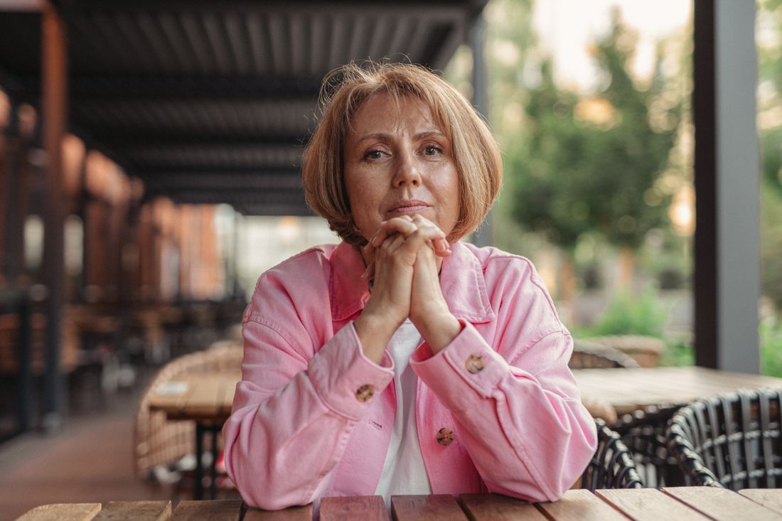 An older woman sitting quietly, hands clasped, lost in thought