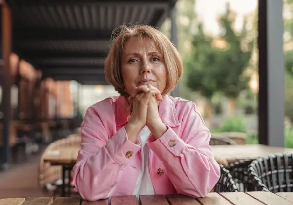 An older woman sitting quietly, hands clasped, lost in thought