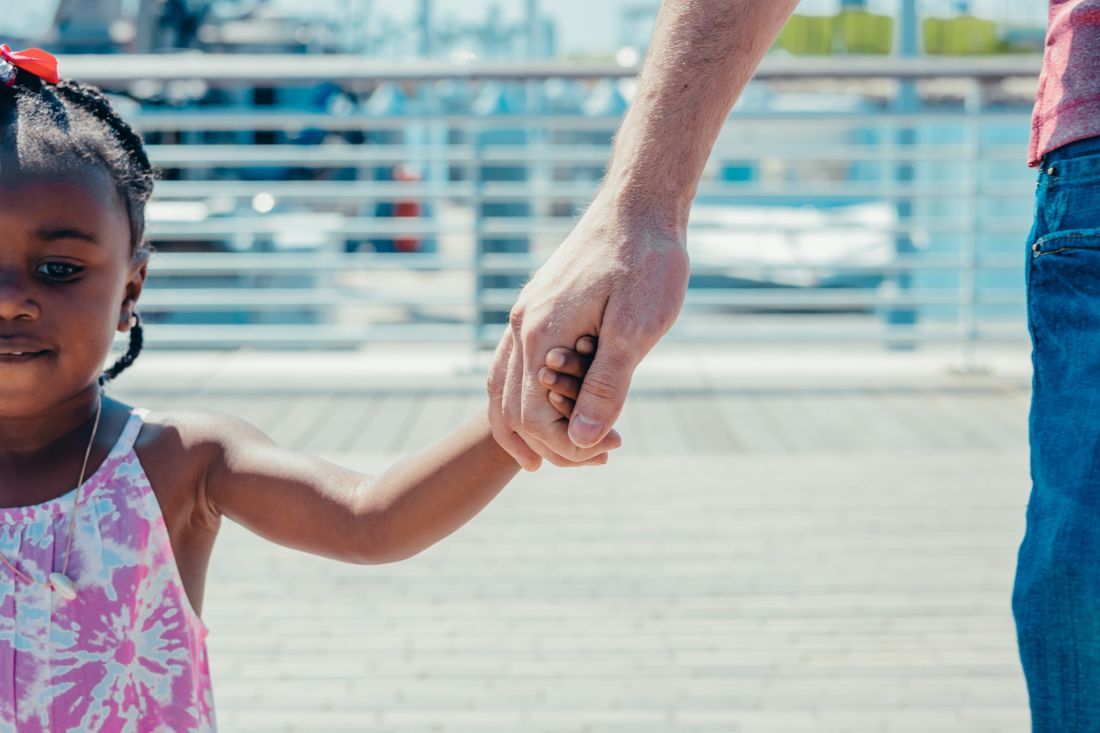 A parent holding a young child's hand on a walk