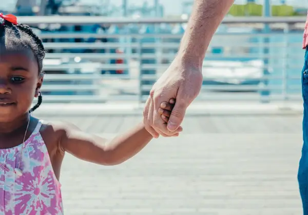 A parent holding a young child's hand on a walk