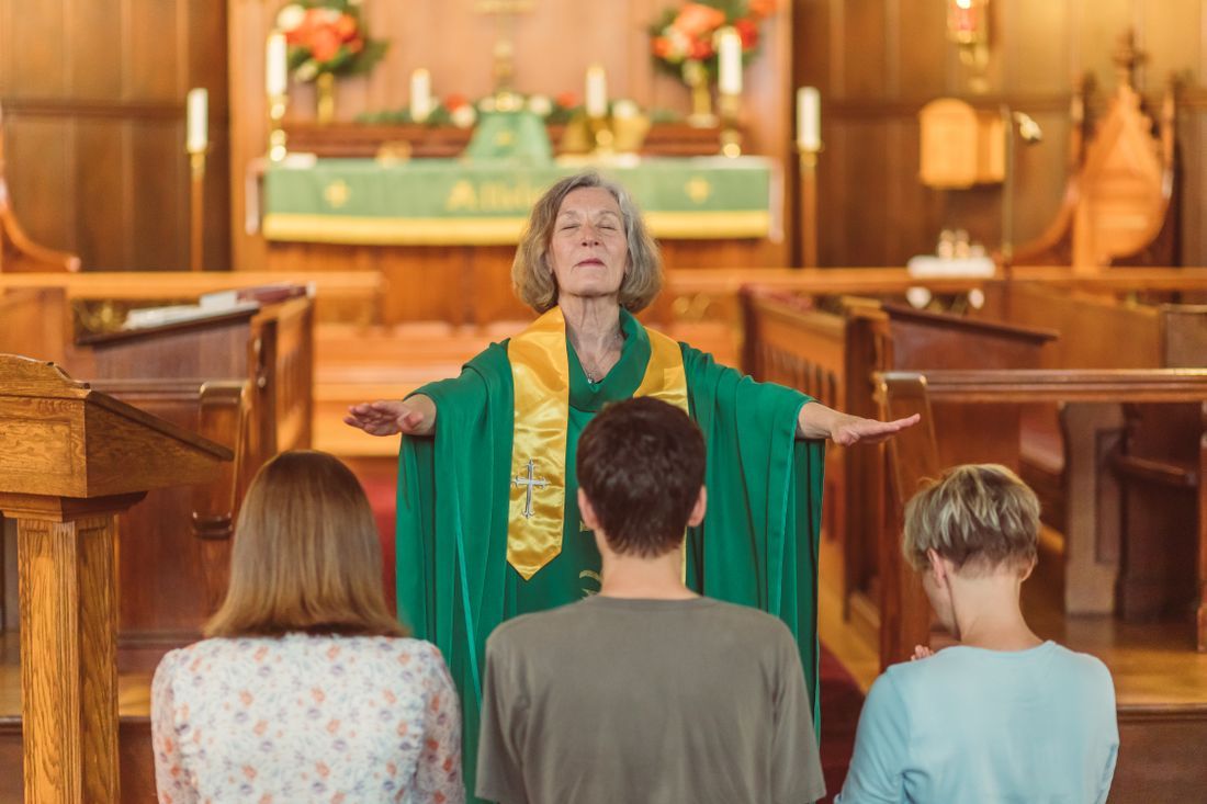 A pastor with arms open in blessing over a kneeling congregation