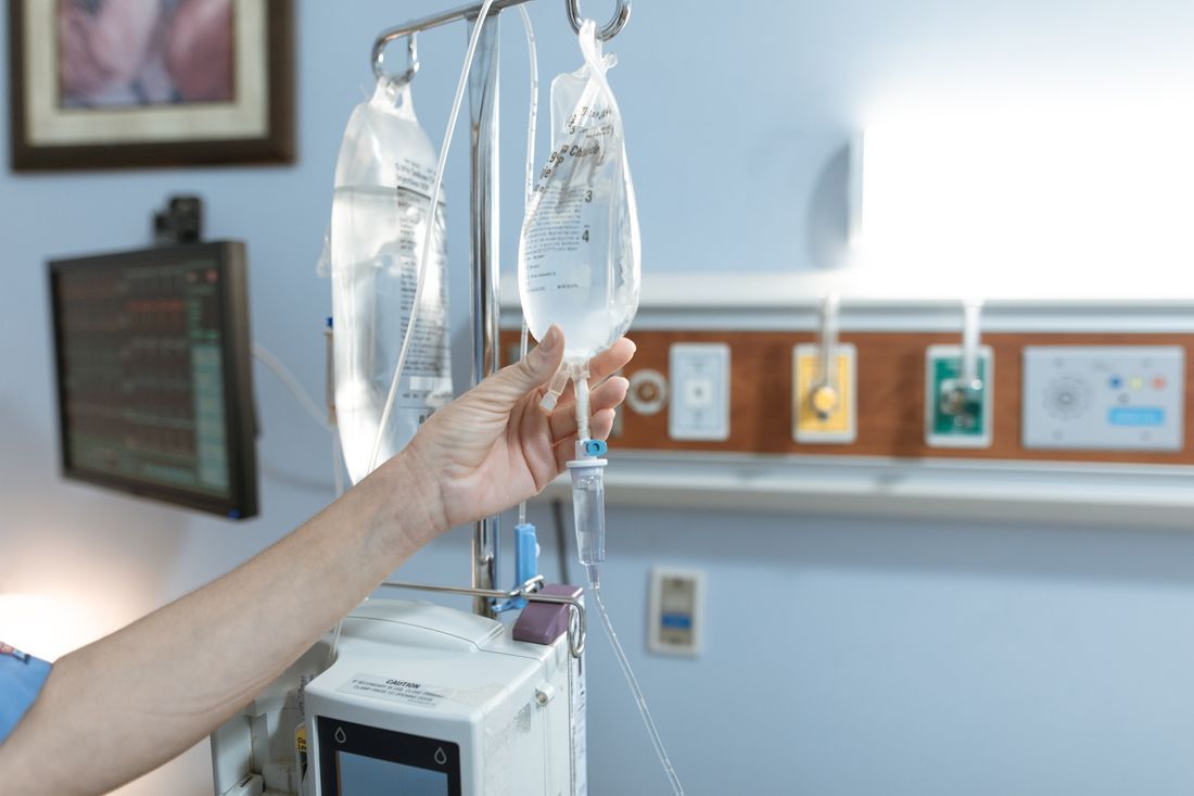 A nurse's hand adjusting an IV drip in a hospital room