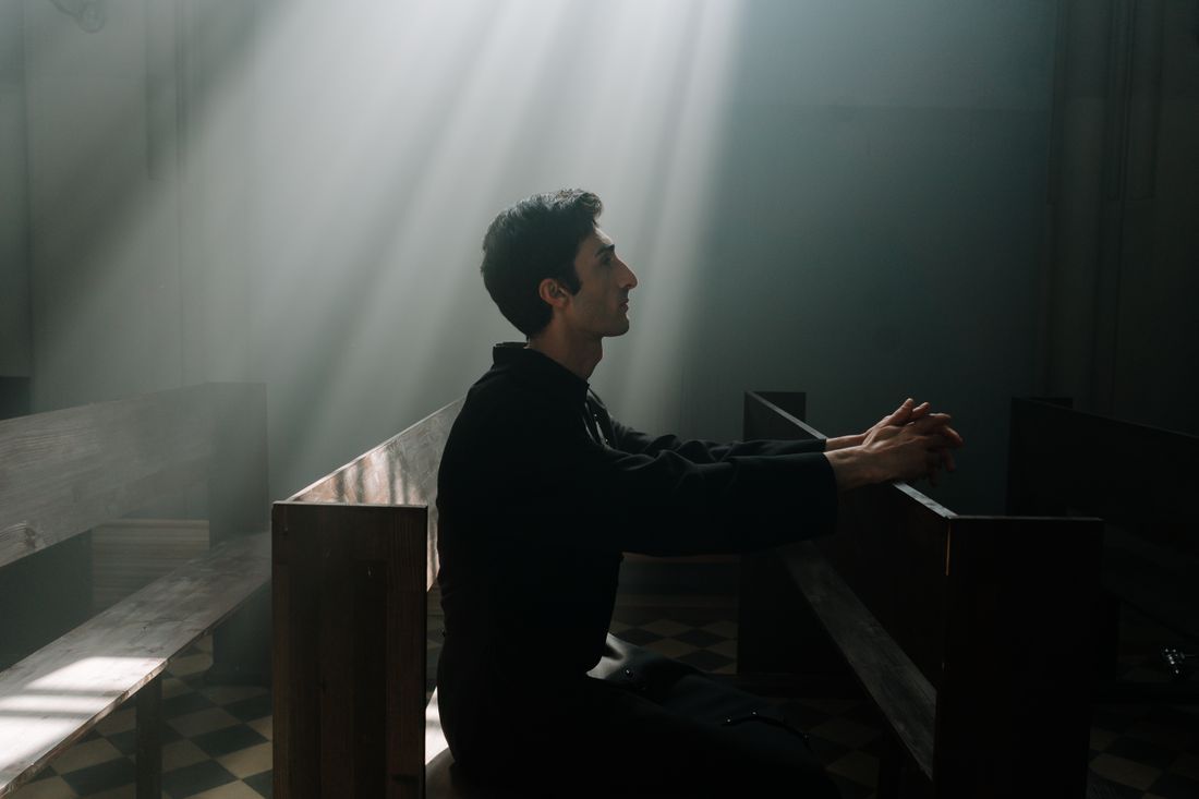 A man praying alone in a shaft of light inside a church