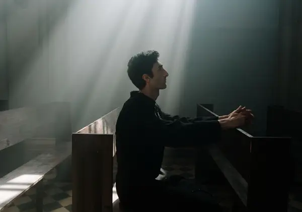 A man praying alone in a shaft of light inside a church