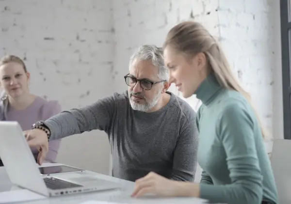 A mentor guiding two colleagues at a laptop