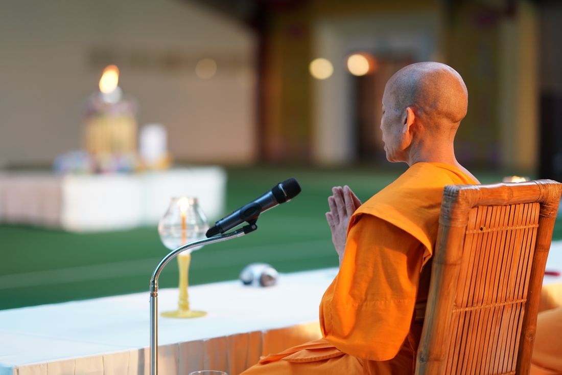A monk with palms together in quiet reverence by a flame