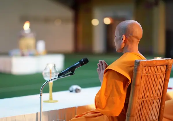 A monk with palms together in quiet reverence by a flame