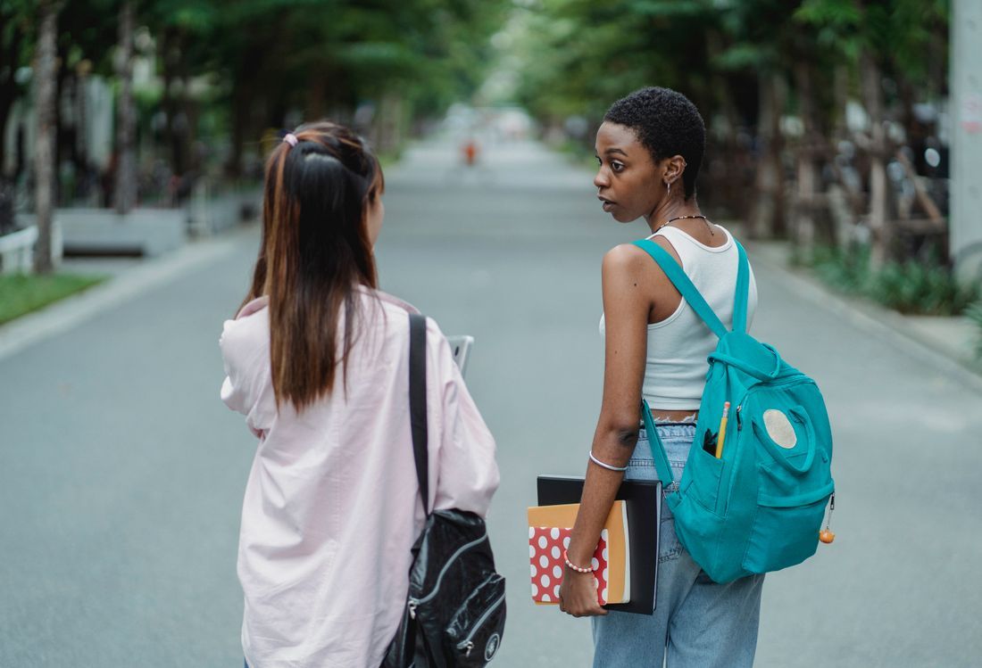 Two college students walking together down a tree-lined campus street