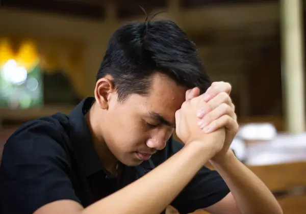 A man sitting alone, head bowed, reaching out for help