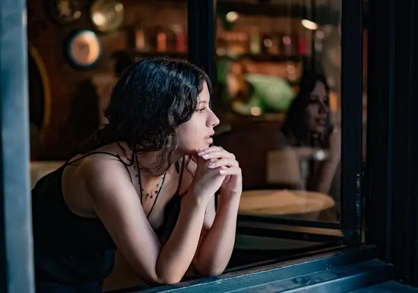 A woman sitting thoughtfully by a window at night