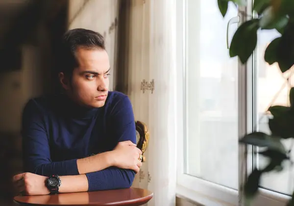 A young man sitting quietly by a window